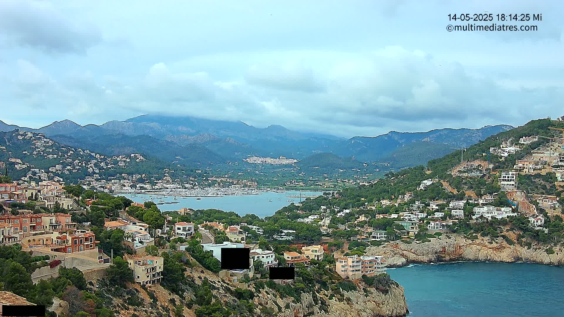 A coastal town nestled in mountains overlooking a calm bay under a partly cloudy sky.