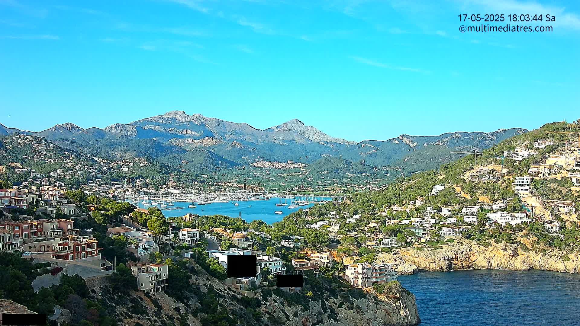 A coastal town nestled between a marina and mountains under a clear blue sky.