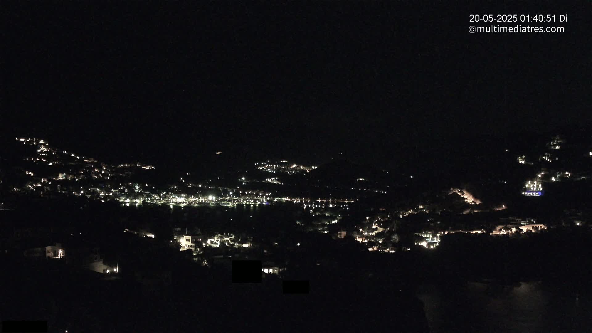 A nighttime view shows a hillside town illuminated by scattered lights, with a dark sky above.