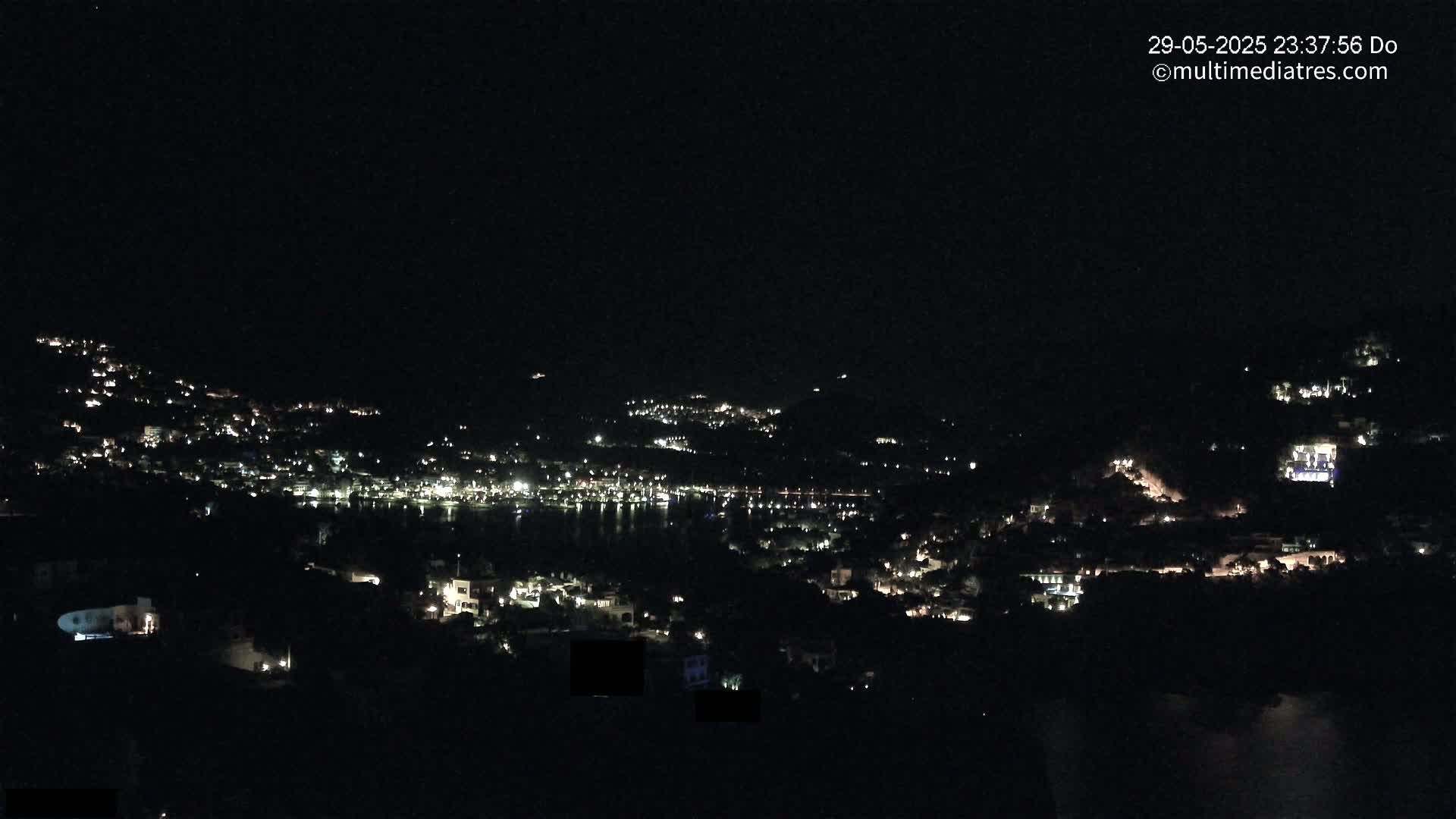 A nighttime view of a coastal town illuminated by scattered lights, set against a dark, clear sky.