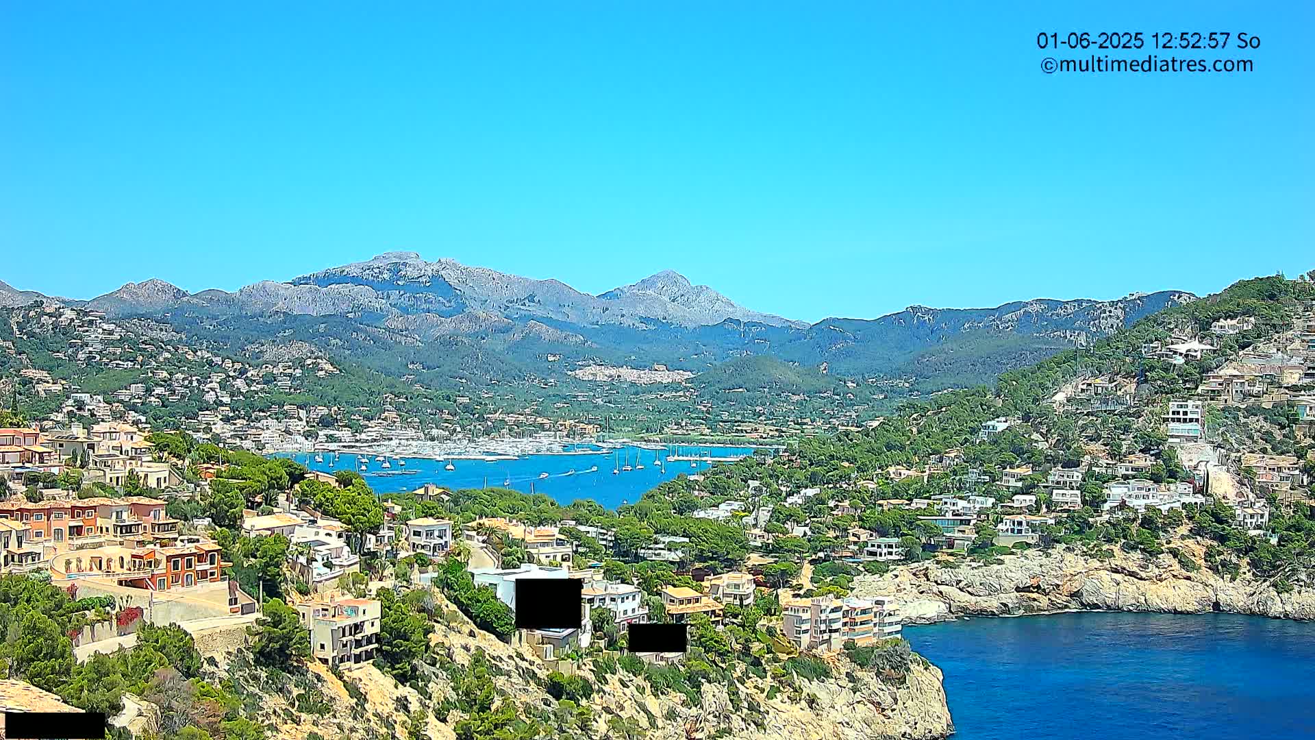 A coastal town nestled against mountains on a clear, sunny day, with a harbor filled with boats.