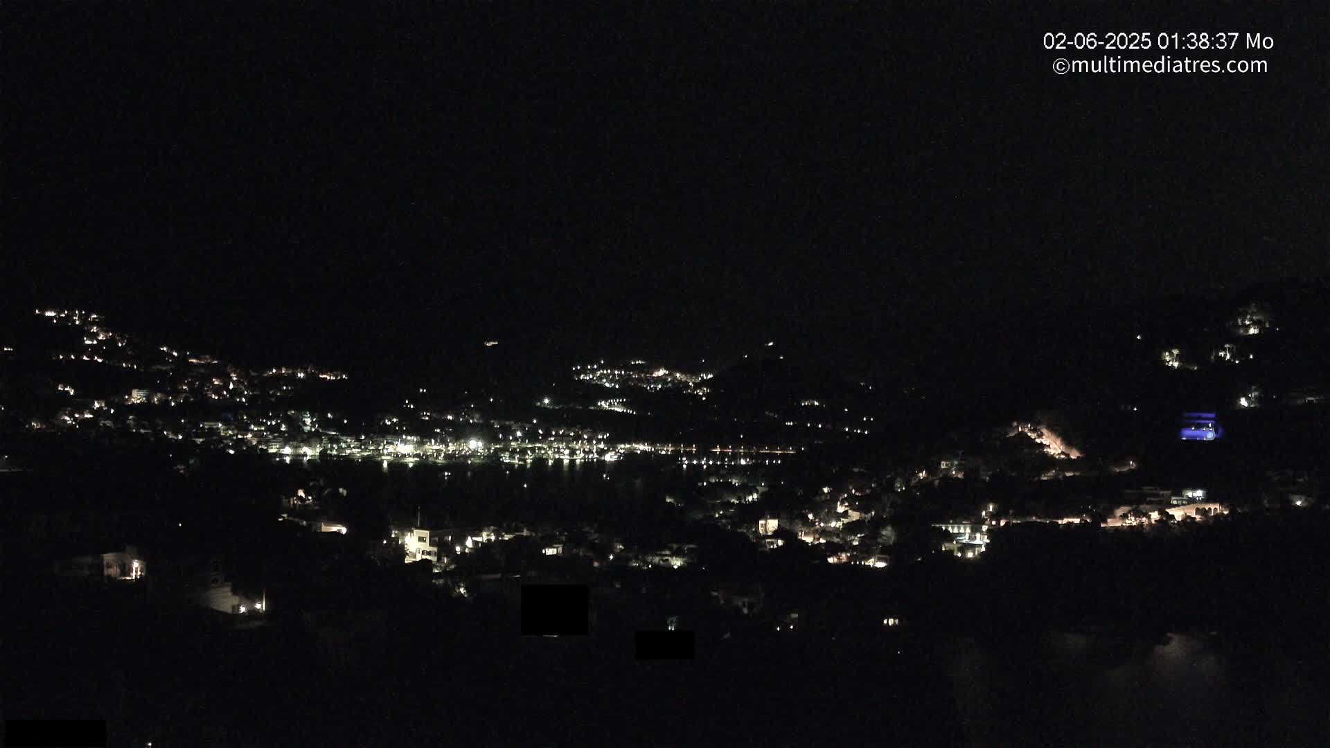 A nighttime view of a town nestled on a hillside, with its lights illuminating the dark landscape.
