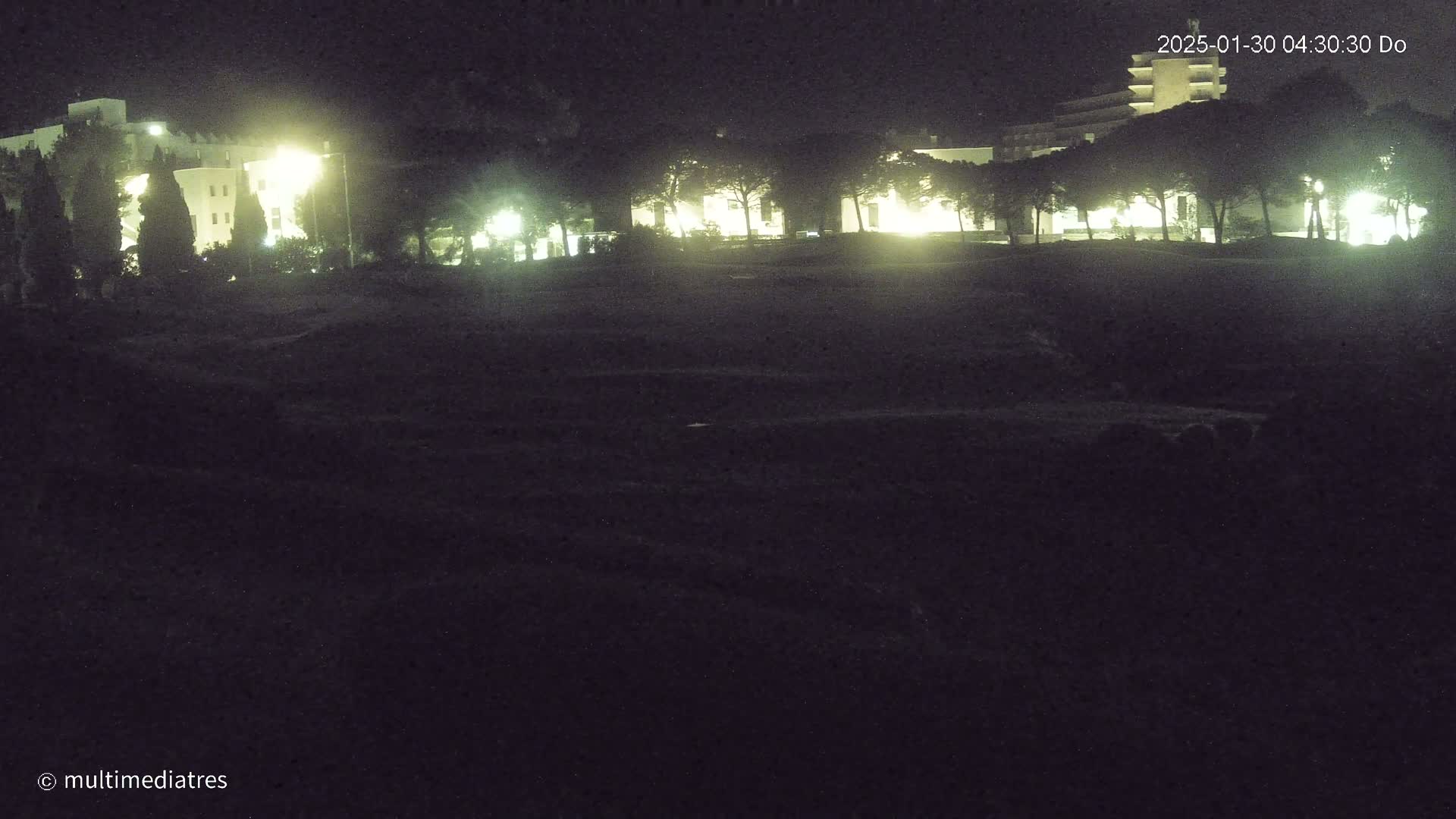 A nighttime view of illuminated buildings and trees, partially obscured by darkness.