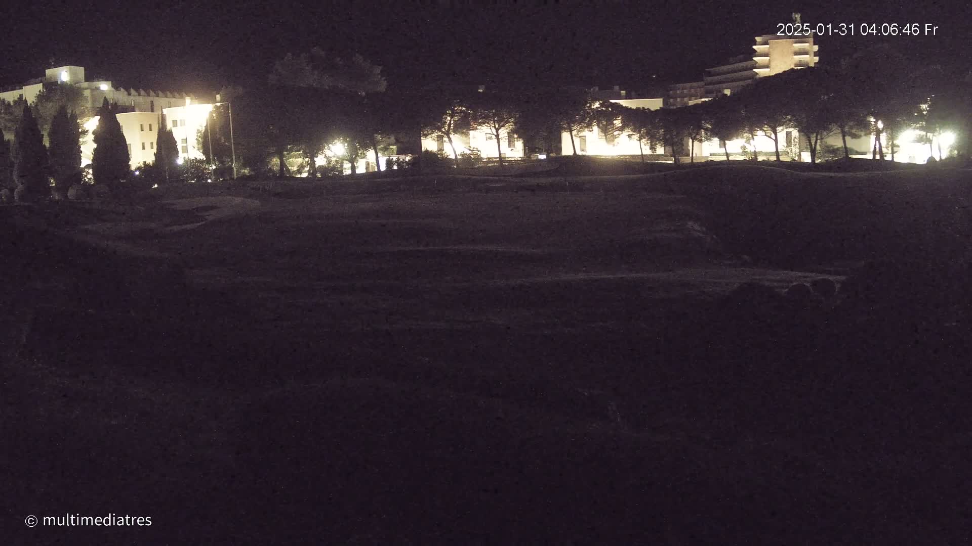 At night, illuminated buildings are visible beyond a dark, grassy area.