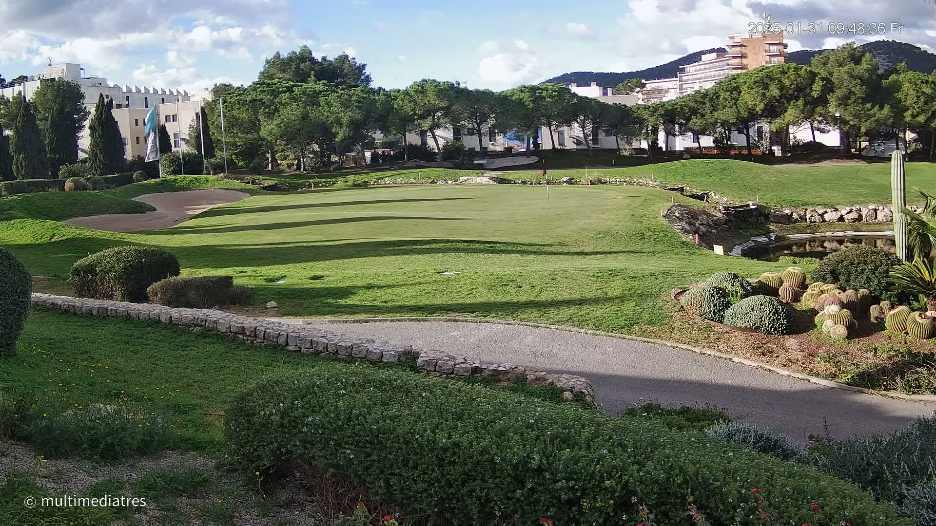 A golf course putting green is visible, with a sand trap and a small pond nearby, under partly cloudy skies.