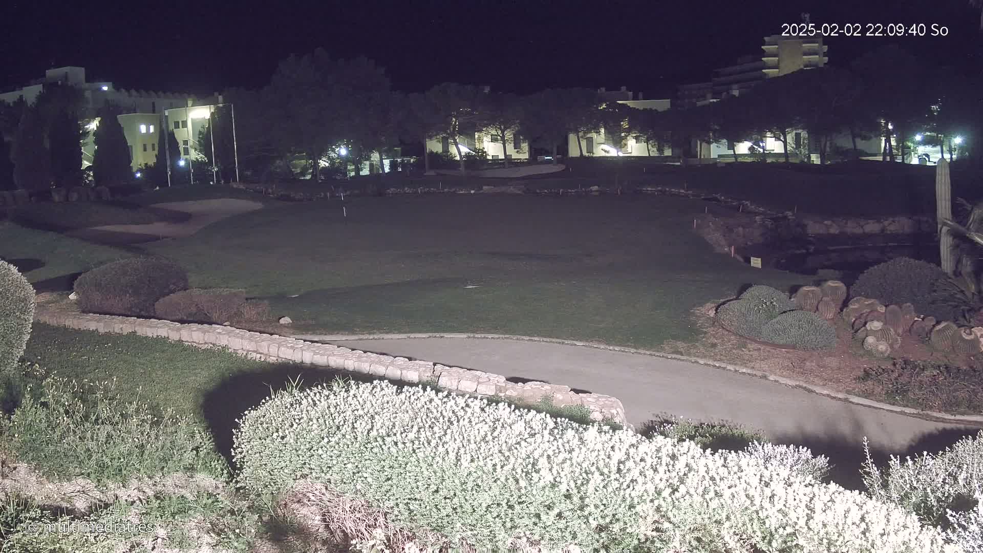 A nighttime view of a golf course with low-lying shrubs and a building in the background under dark conditions.