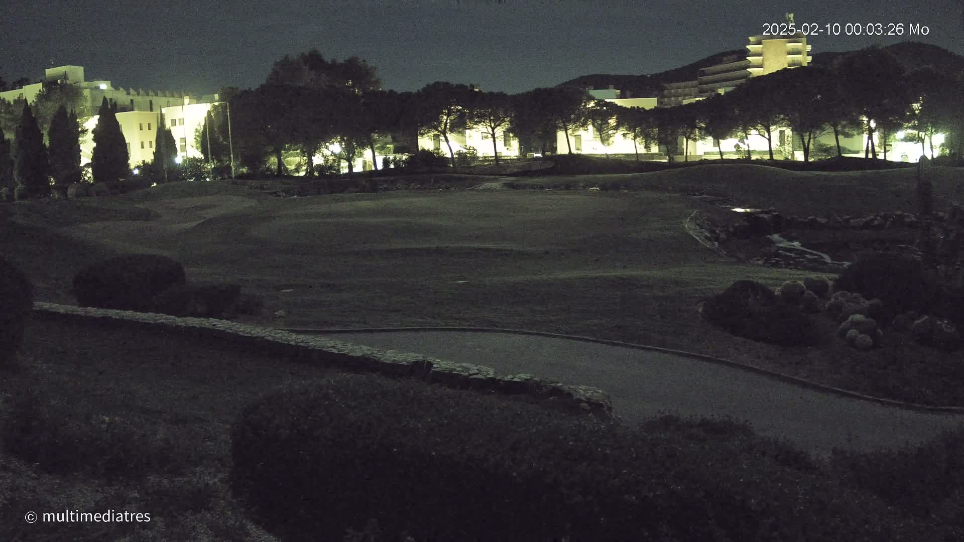 A nighttime view of a golf course with illuminated buildings in the background under a dark sky.