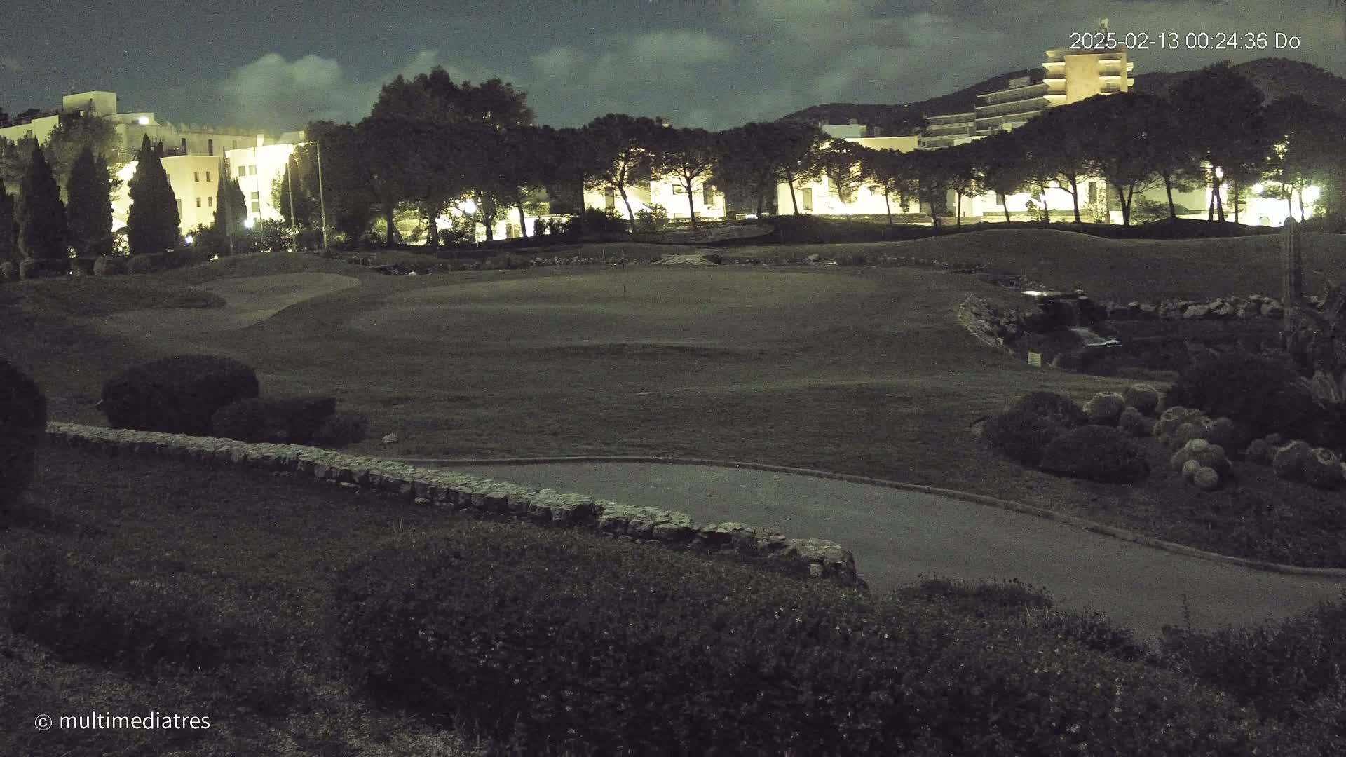 A nighttime view of a golf course with a building in the background under a partly cloudy sky.