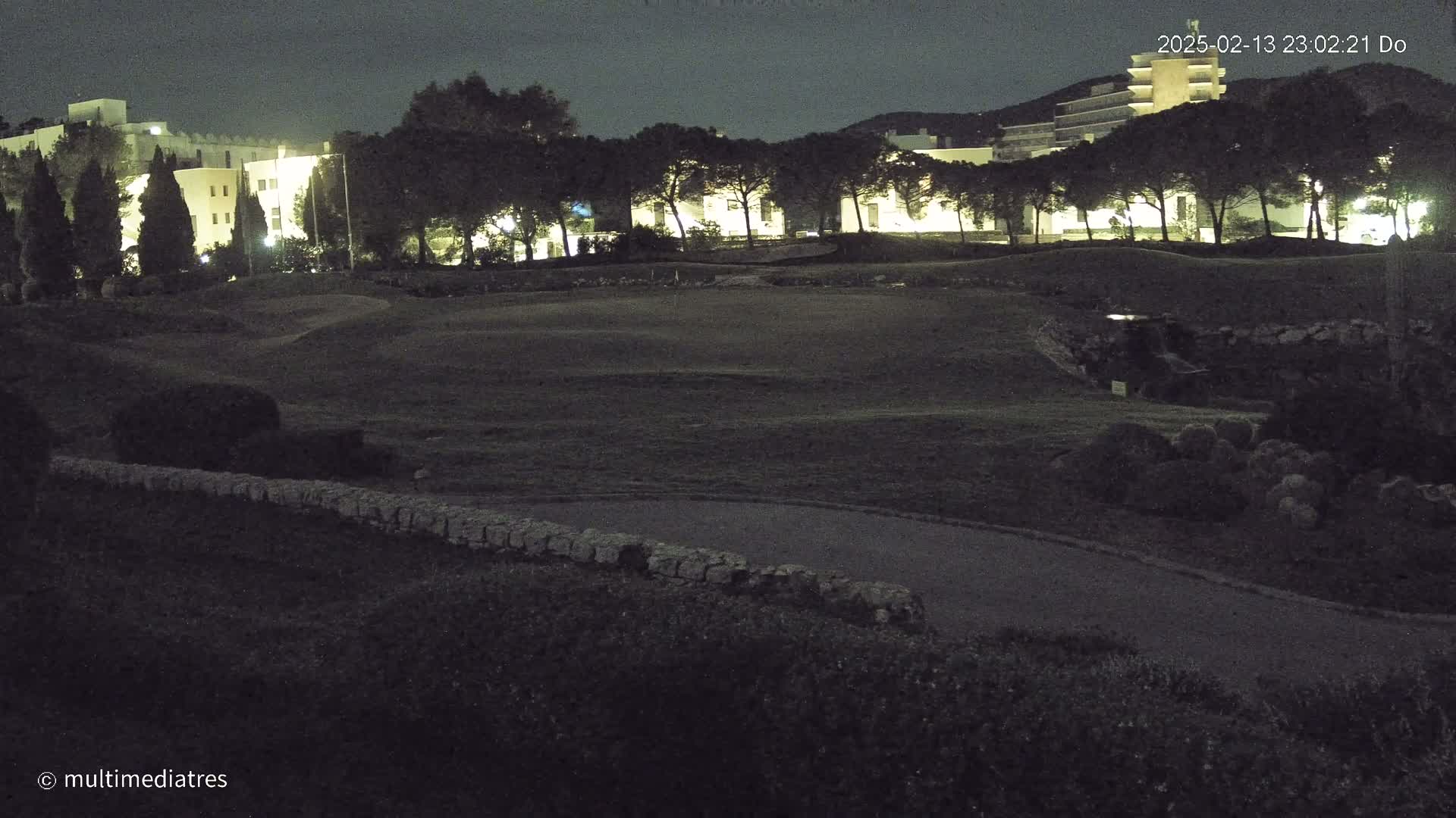 A nighttime view of a grassy area with illuminated buildings in the background under a dark sky.