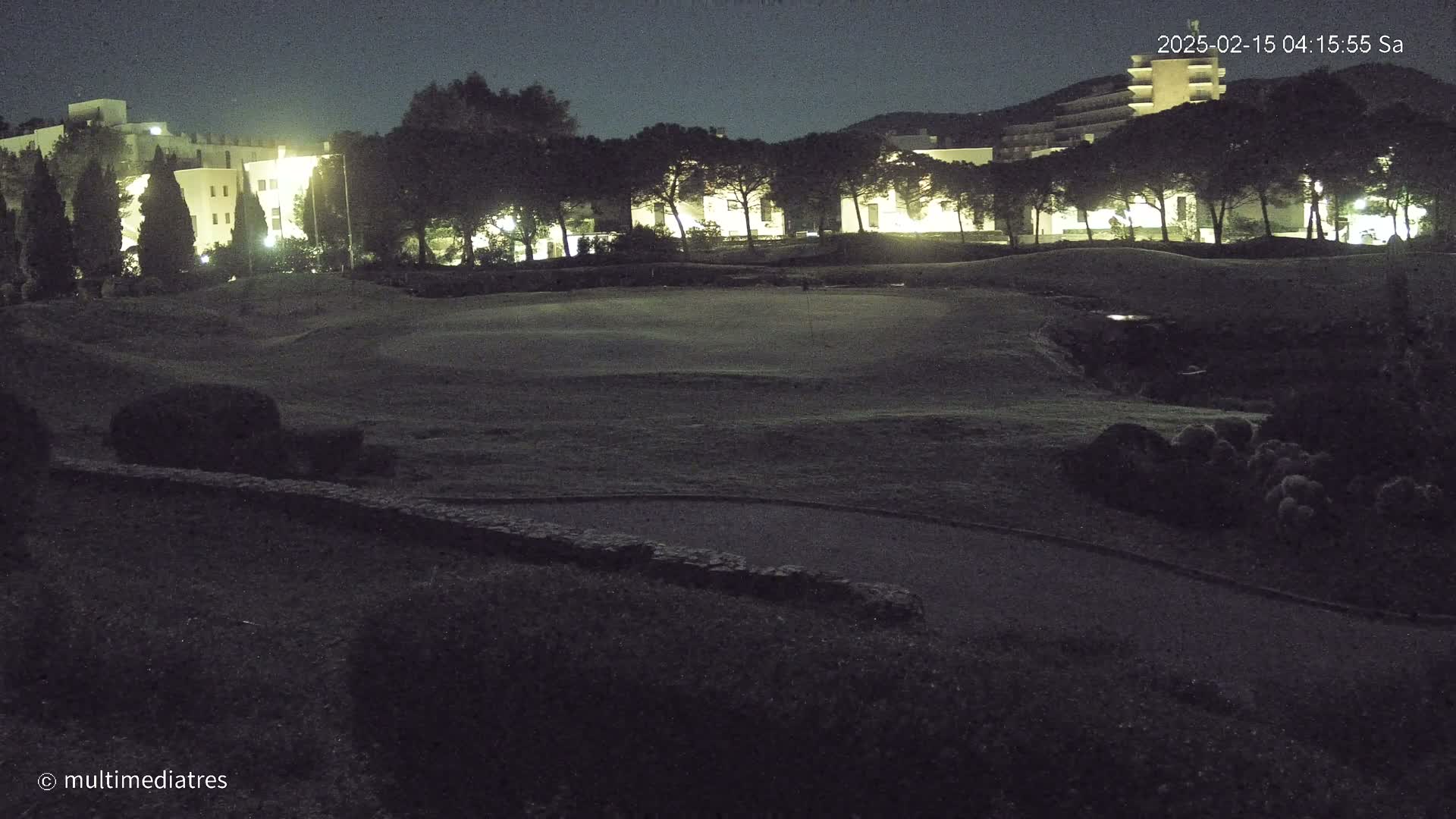 A nighttime view of a golf course with illuminated buildings in the background under a dark sky.
