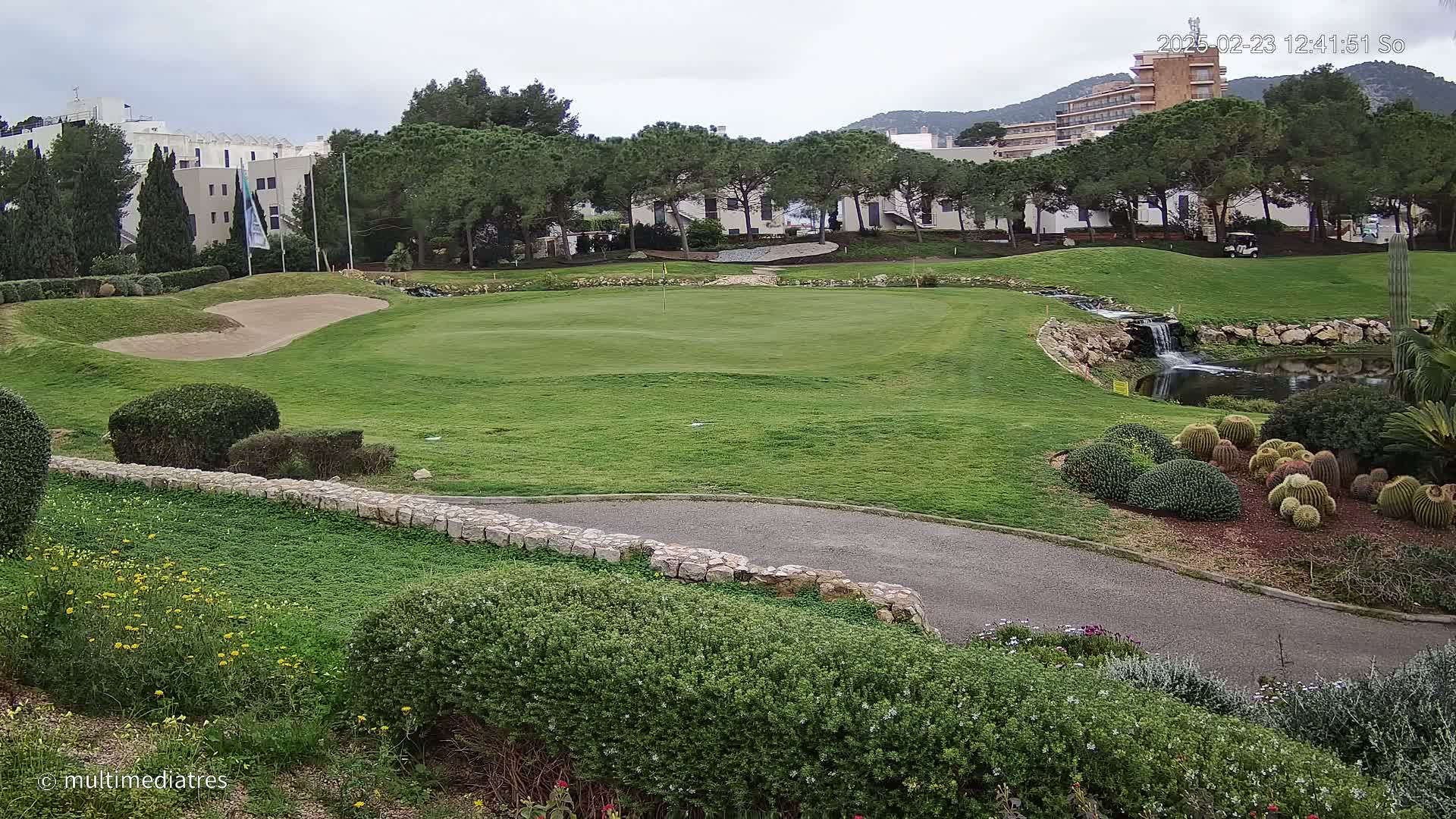 A golf course with a green, sand trap, and small waterfall under an overcast sky.