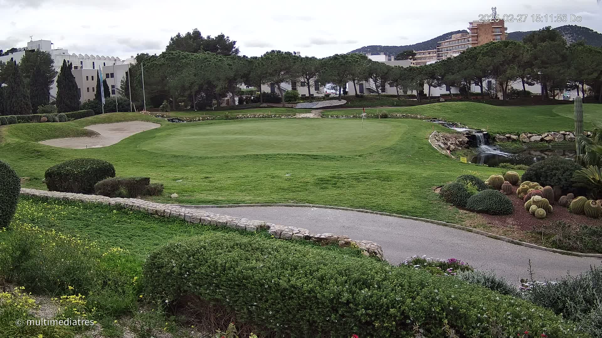 A golf course green with a sand trap, a small waterfall, and numerous cacti is visible, under a cloudy sky.
