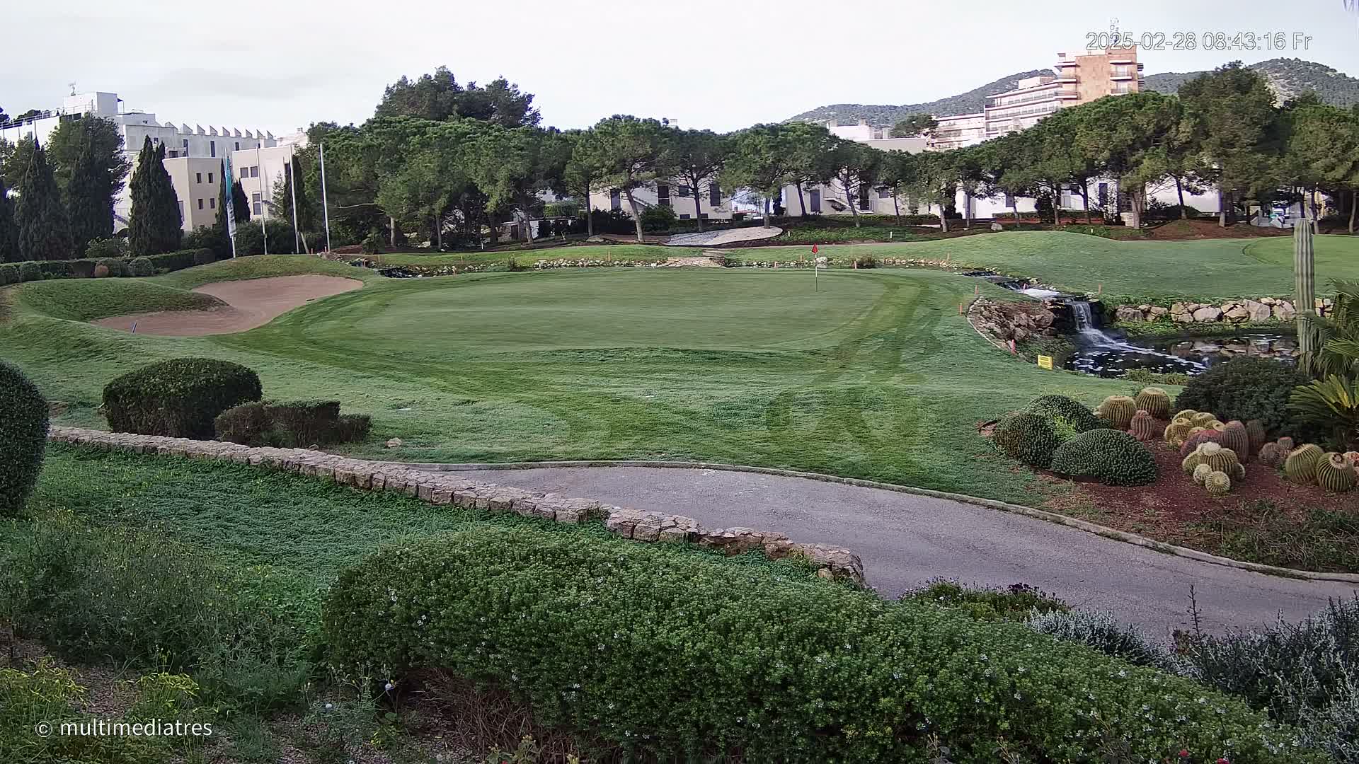 A golf course green with a sand trap, a small waterfall, and a collection of cacti is visible, under a partly cloudy sky.