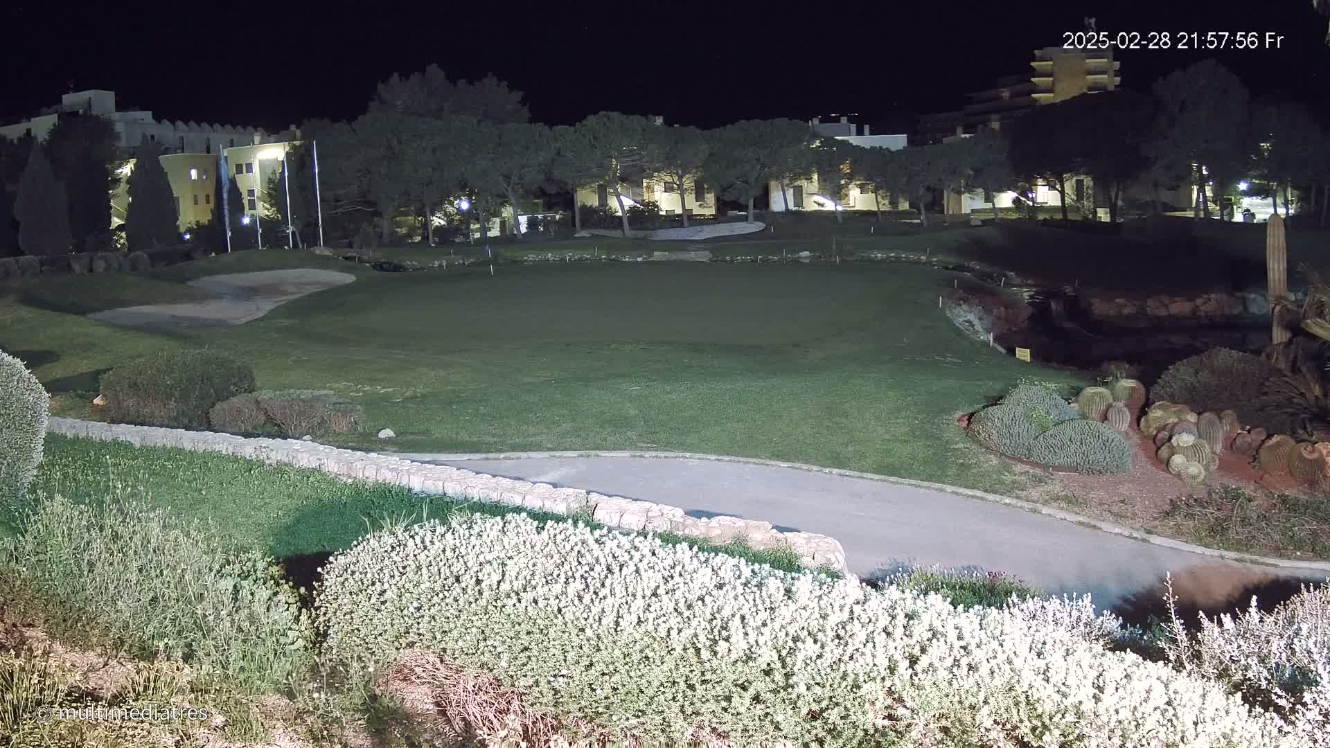A nighttime view of a golf course with a building in the background, illuminated by artificial lights.