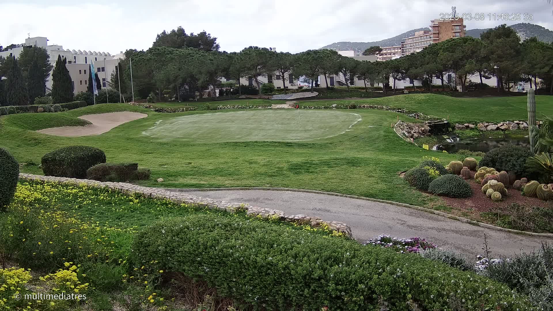 A golf course putting green with sand traps and manicured landscaping is visible under an overcast sky, with a hotel and trees in the background.