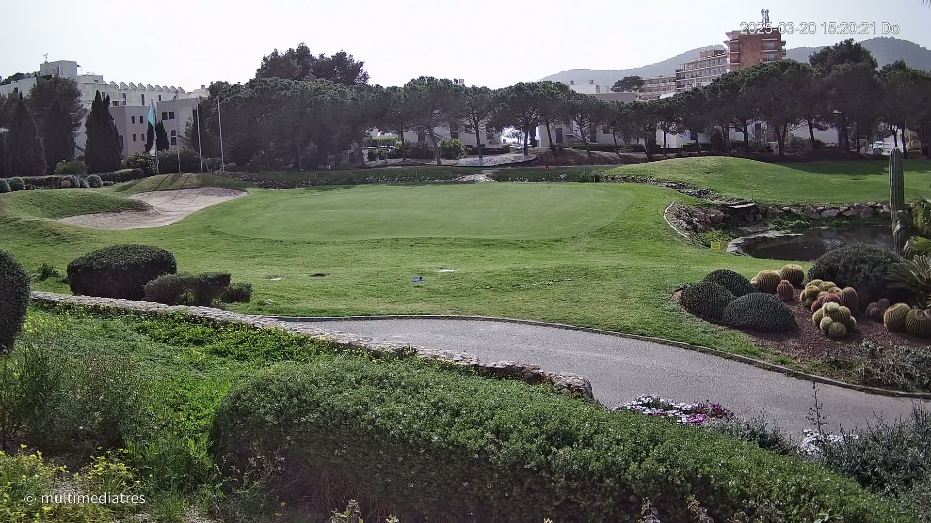 A golf course green with sand traps and surrounding landscaping is visible under a partly cloudy sky, with buildings and trees in the background.