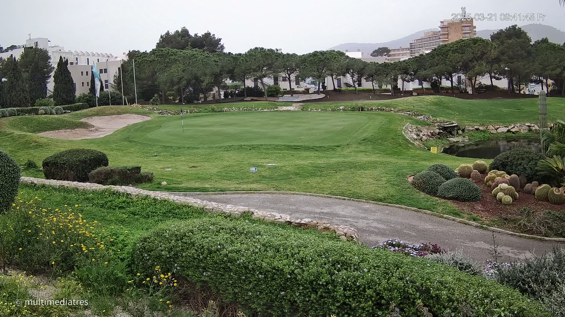 A golf course green with sand traps and a small pond is visible, situated near a building complex under an overcast sky.