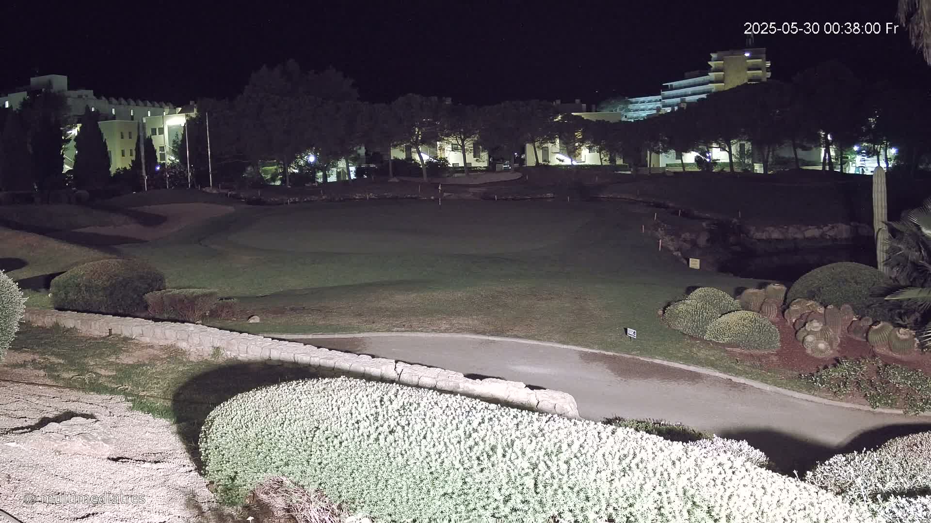 A nighttime view of a golf course next to buildings under artificial light.
