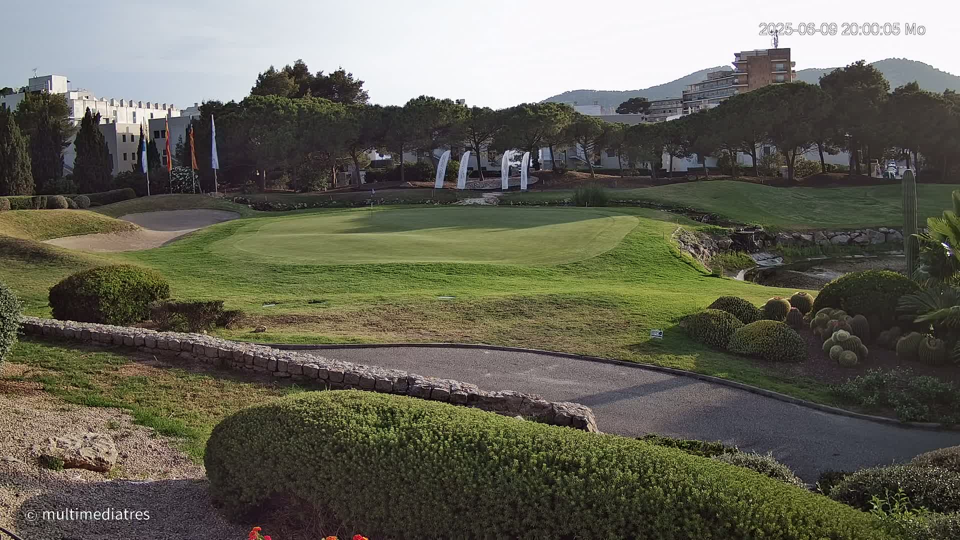 A golf course green, sand trap, and landscaping are visible under a clear sky, with buildings and trees in the background.