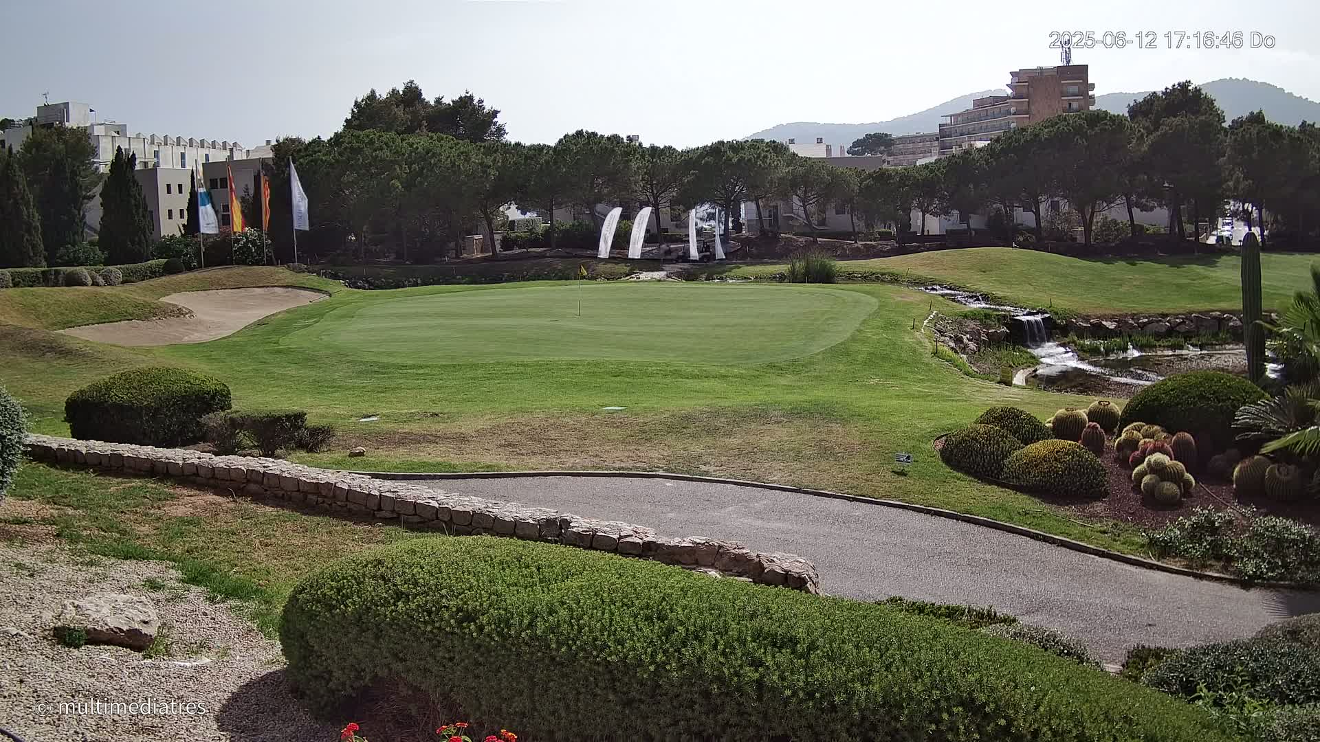 A golf course putting green with a small waterfall and manicured landscaping is visible under sunny skies.