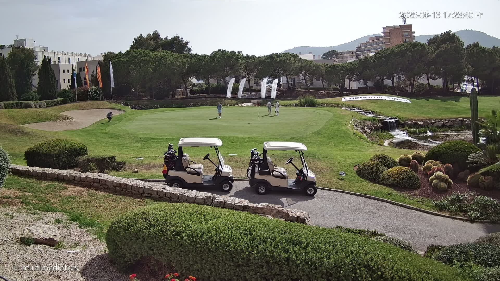 Two golf carts are parked near a green golf course with several golfers in the distance under a mostly sunny sky.