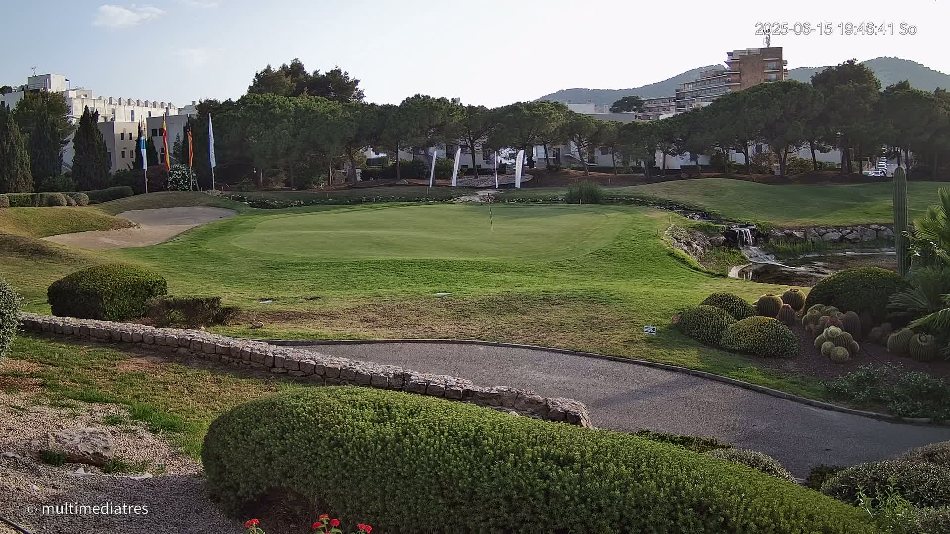A green golf course with a sand trap, a small waterfall, and lush landscaping under a clear sky.