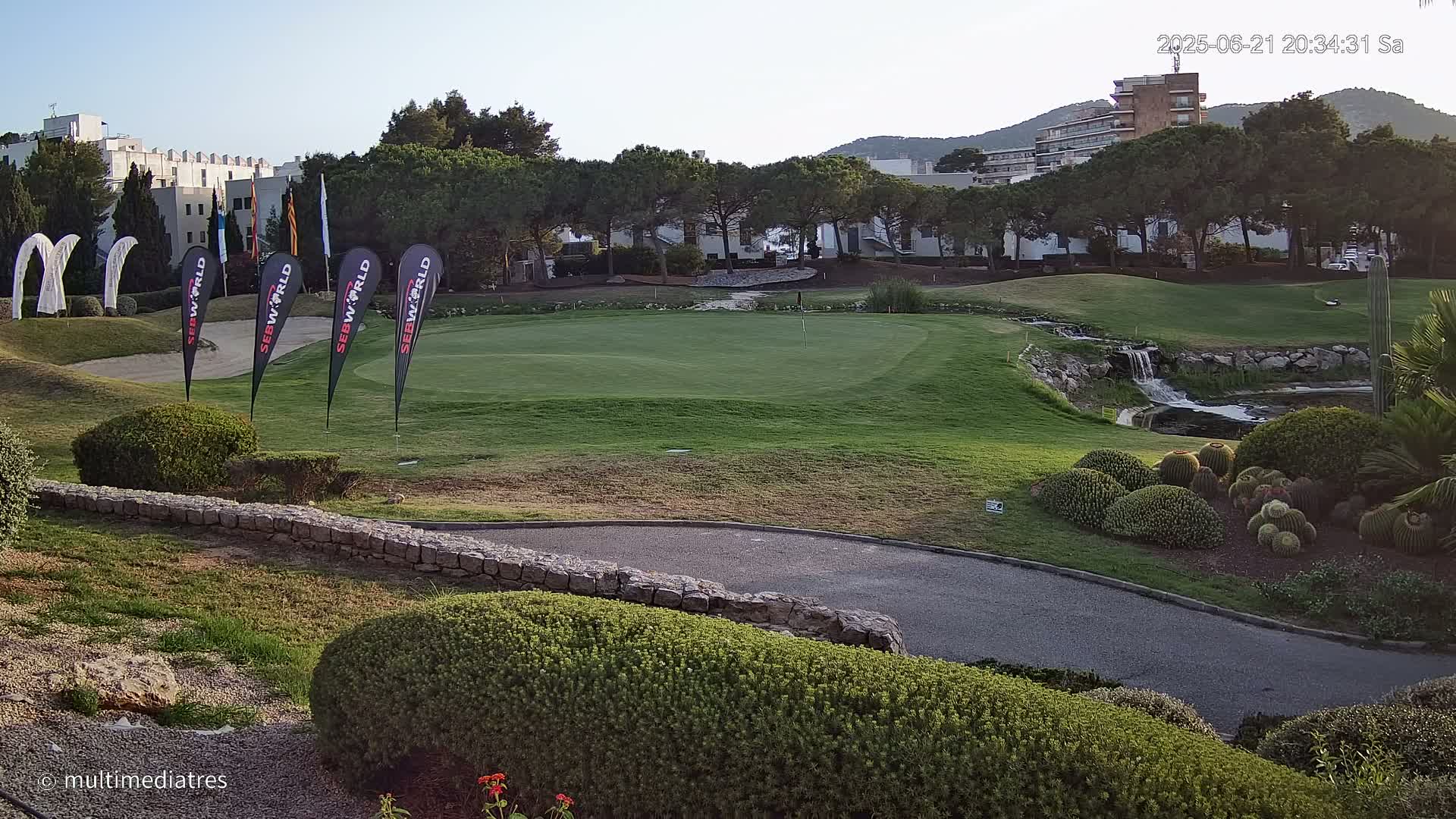 A putting green on a golf course with a small waterfall and cacti under a clear sky.