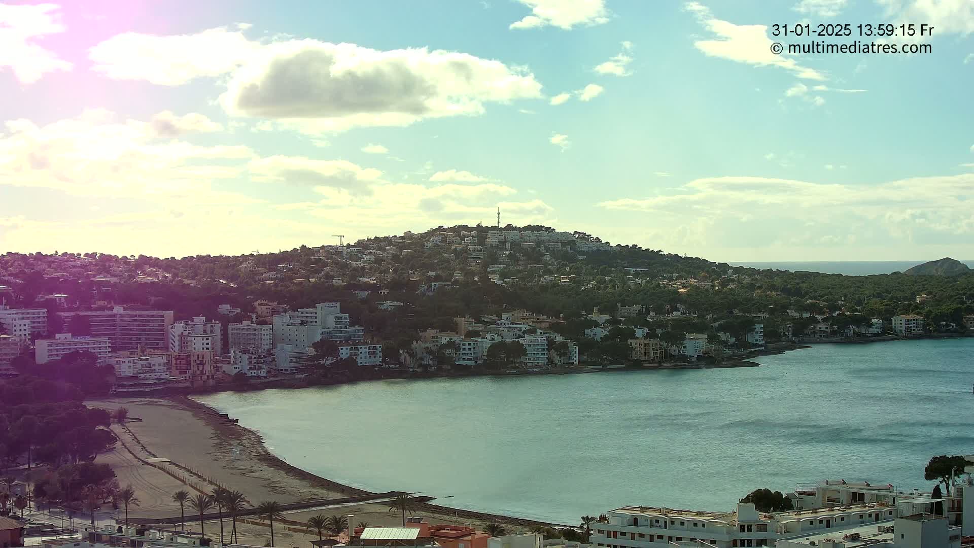 A coastal town nestled on a hillside, with a partly cloudy sky and calm sea, is visible from an elevated viewpoint.