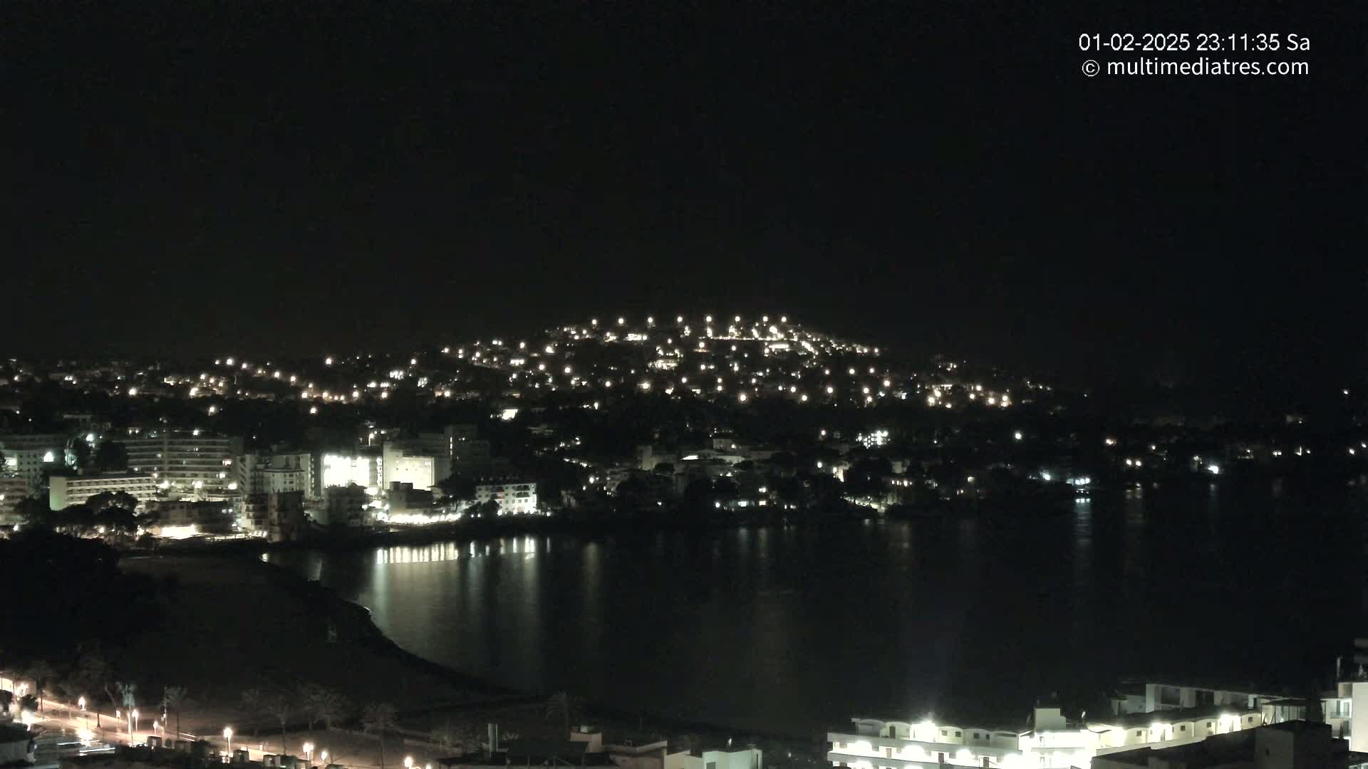 A nighttime view of a city and calm body of water, illuminated by many lights.