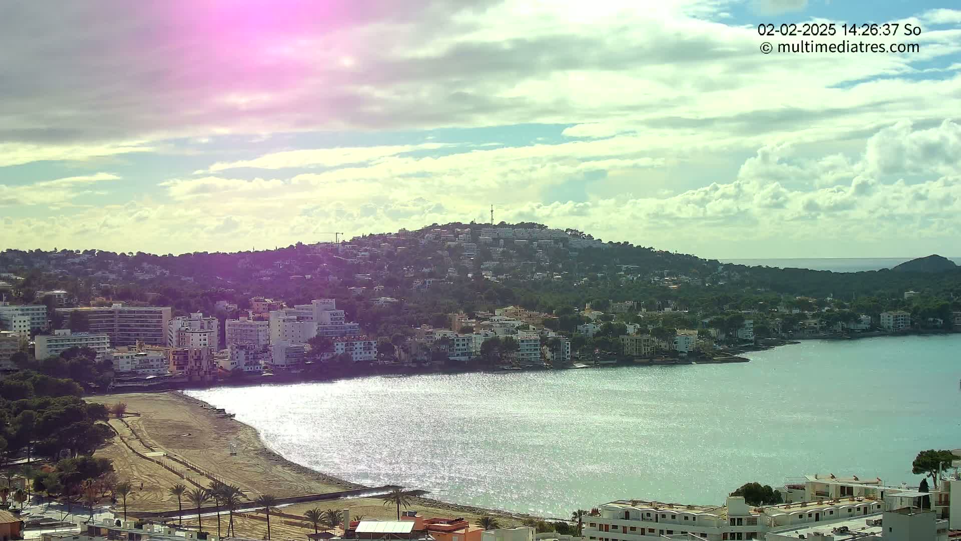 A coastal town with buildings lining a calm bay under a partly cloudy sky.
