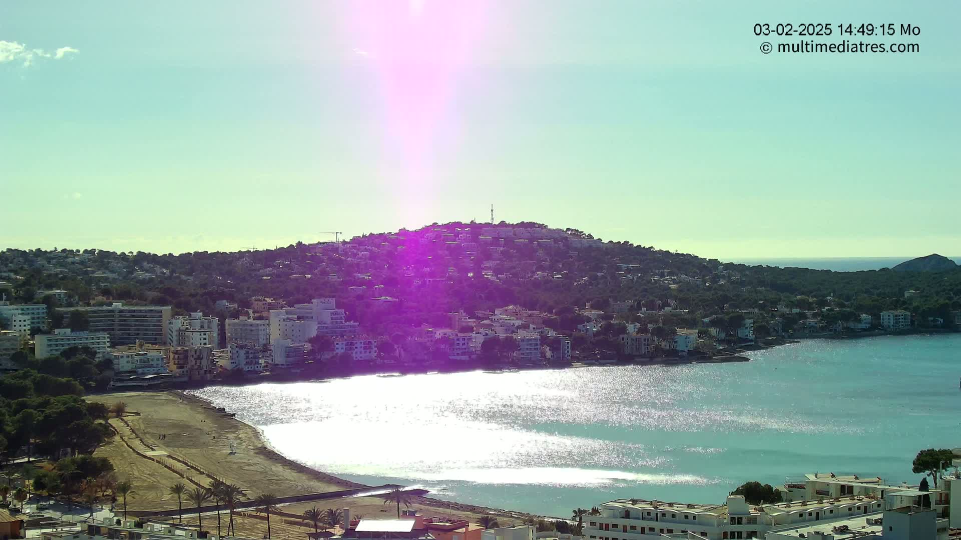 A bright, sunny day reveals a coastal town nestled against a hillside overlooking a sparkling bay.