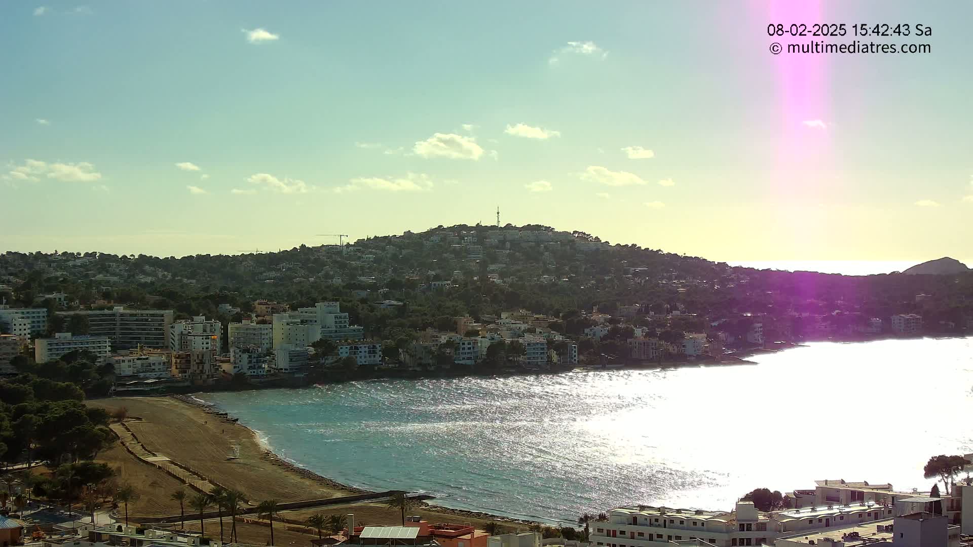 A coastal town nestled on a hill overlooking a sparkling sea under a partly cloudy sky.