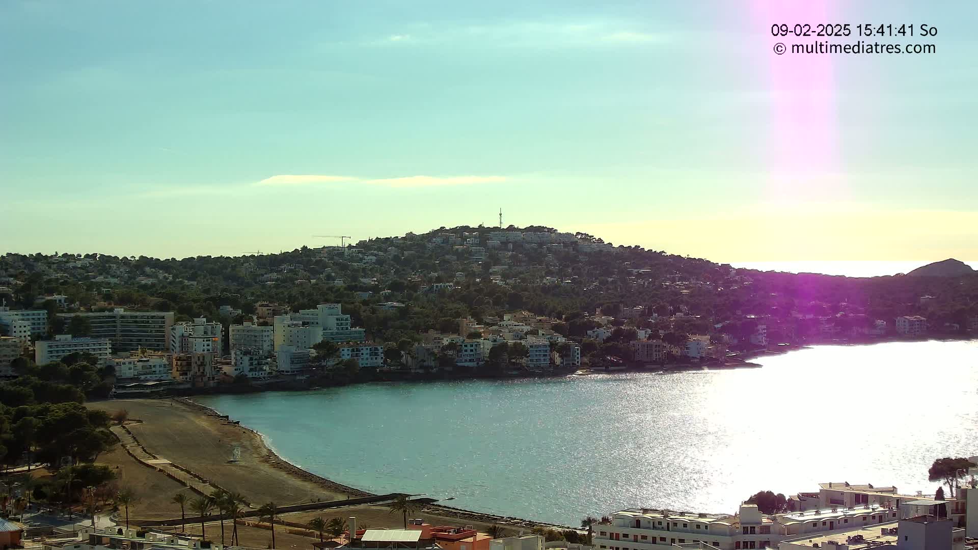 A coastal town nestled on a hillside overlooking a calm, sunlit bay under a clear sky.