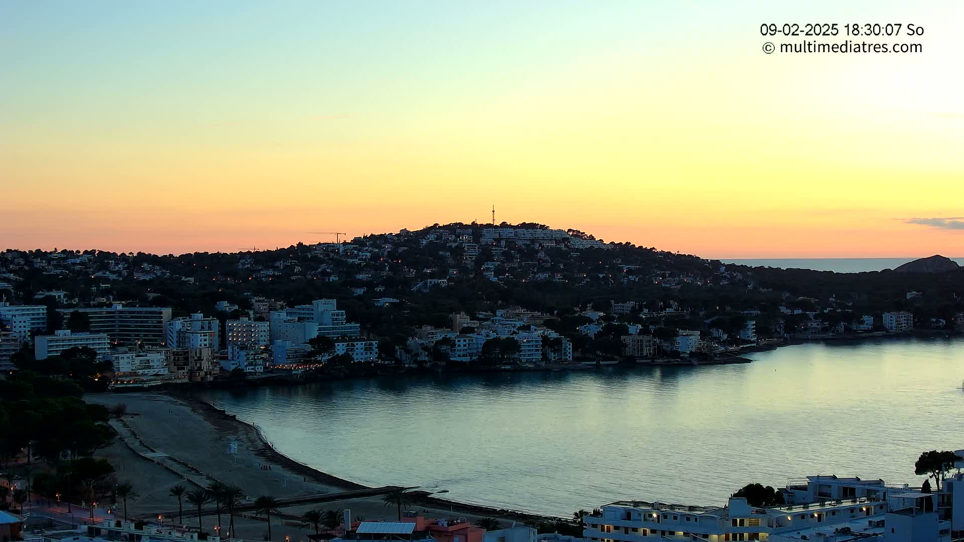 A coastal town nestled on a hill overlooking a calm bay at sunset.