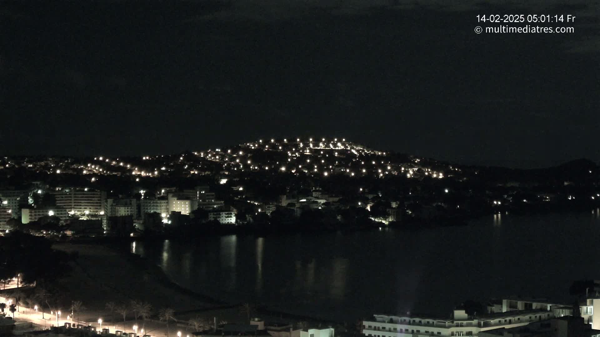 A nighttime view of a city illuminated by lights on a hill overlooking a dark body of water.