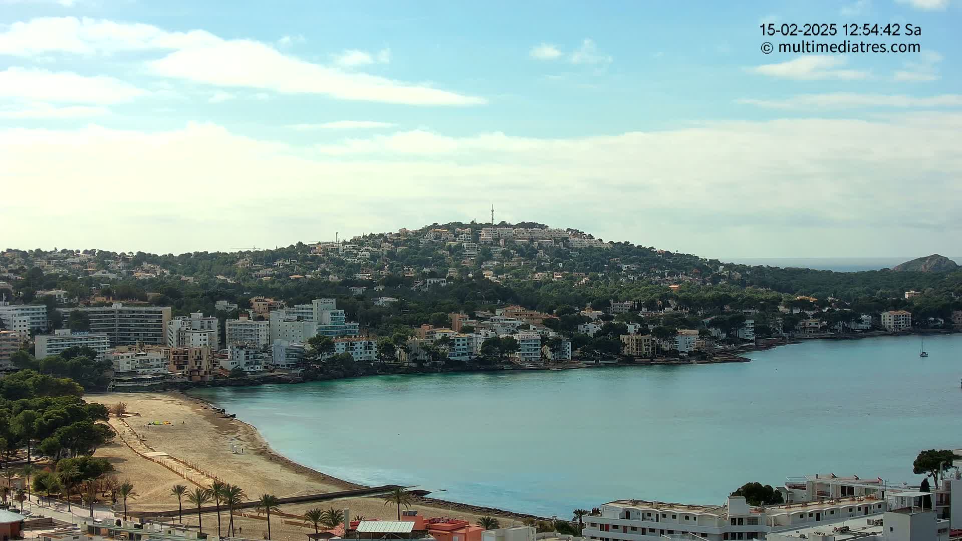 A coastal town with buildings clustered around a bay under a partly cloudy sky.