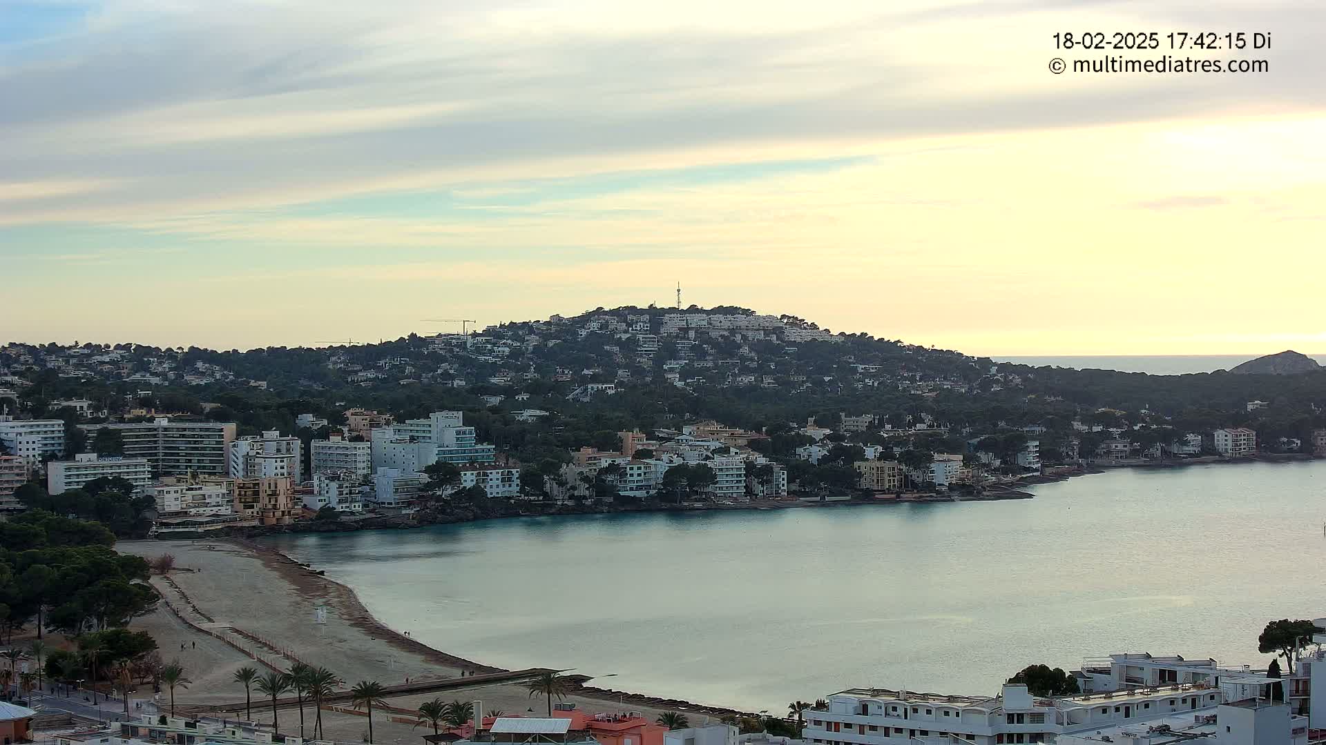 A coastal town with buildings clustered around a calm bay under a partly cloudy sunset sky.