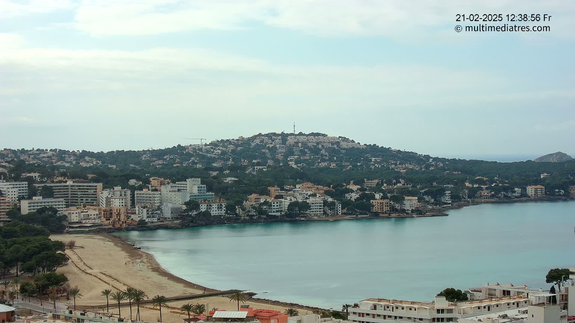 A coastal town with buildings clustered around a calm bay, under a mostly cloudy sky.