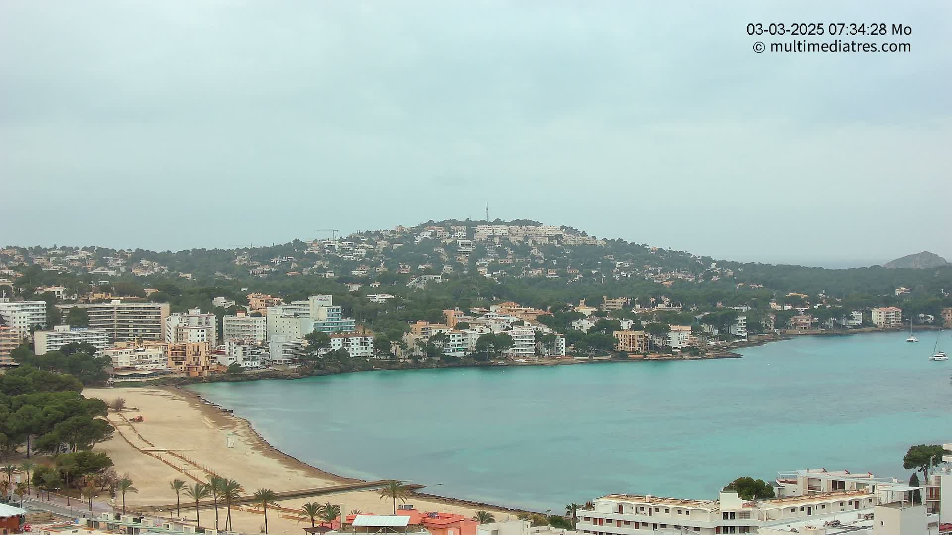 A coastal town with a sandy beach and turquoise water under an overcast sky.