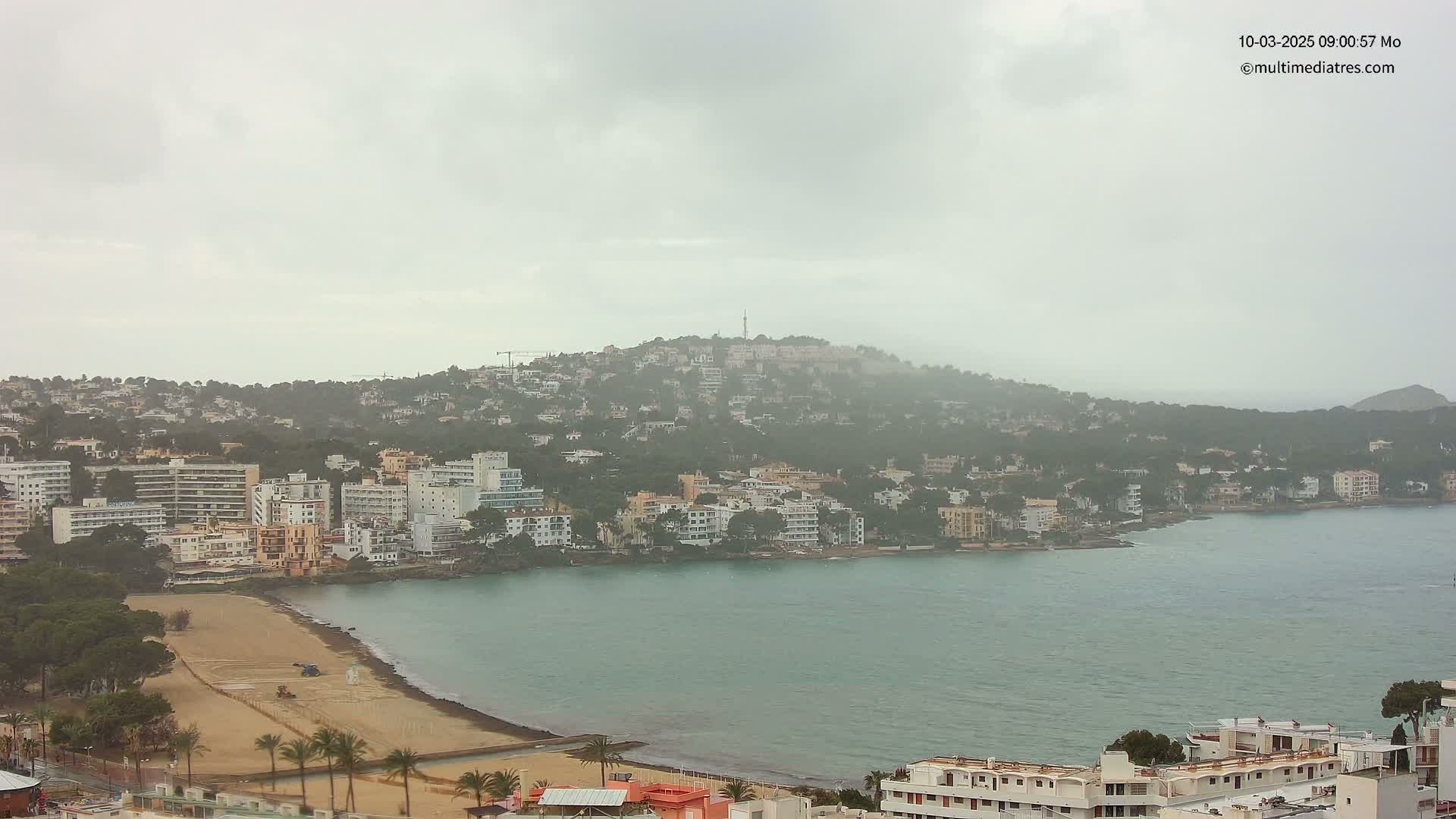 A coastal town with many buildings sits on a bay under an overcast, hazy sky.