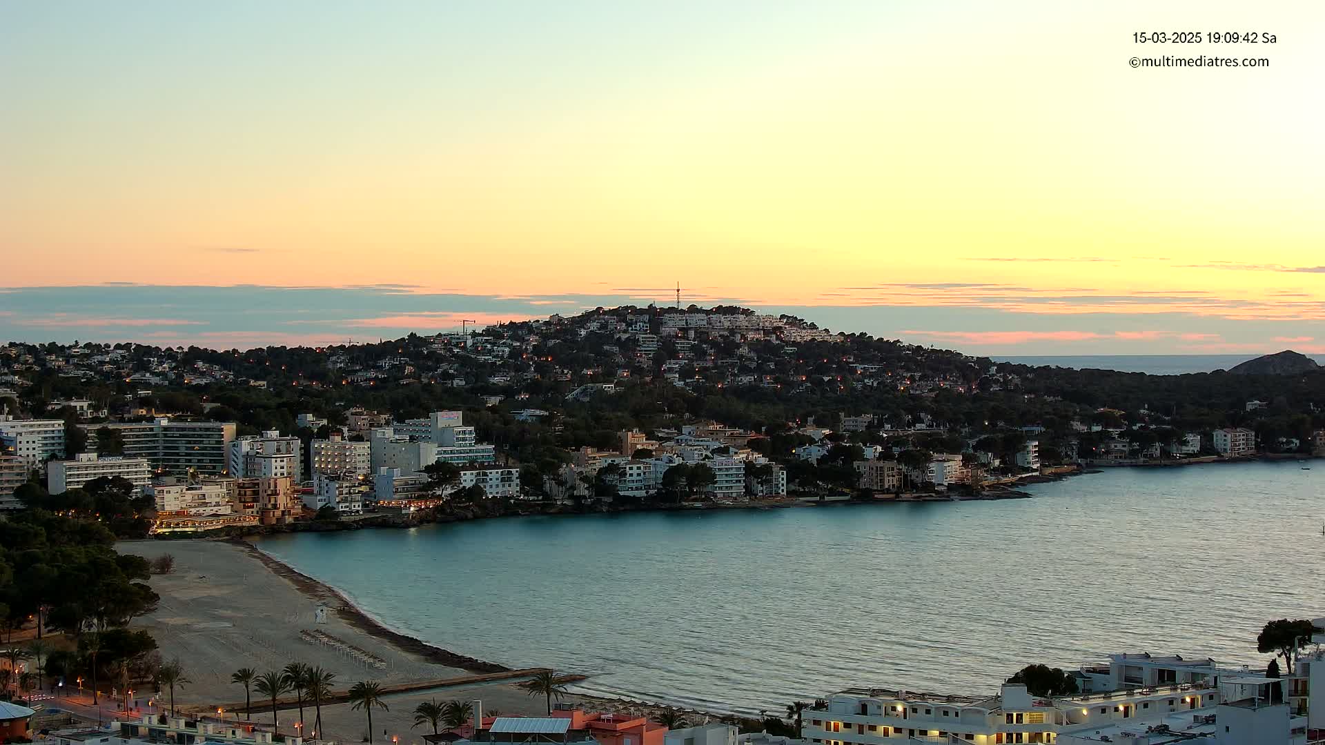 A coastal town nestled on a hill overlooking a calm bay at sunset.