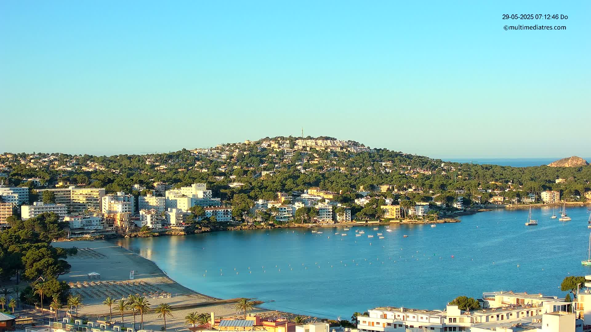 A coastal town nestled on a hillside overlooking a calm bay on a clear, sunny day.