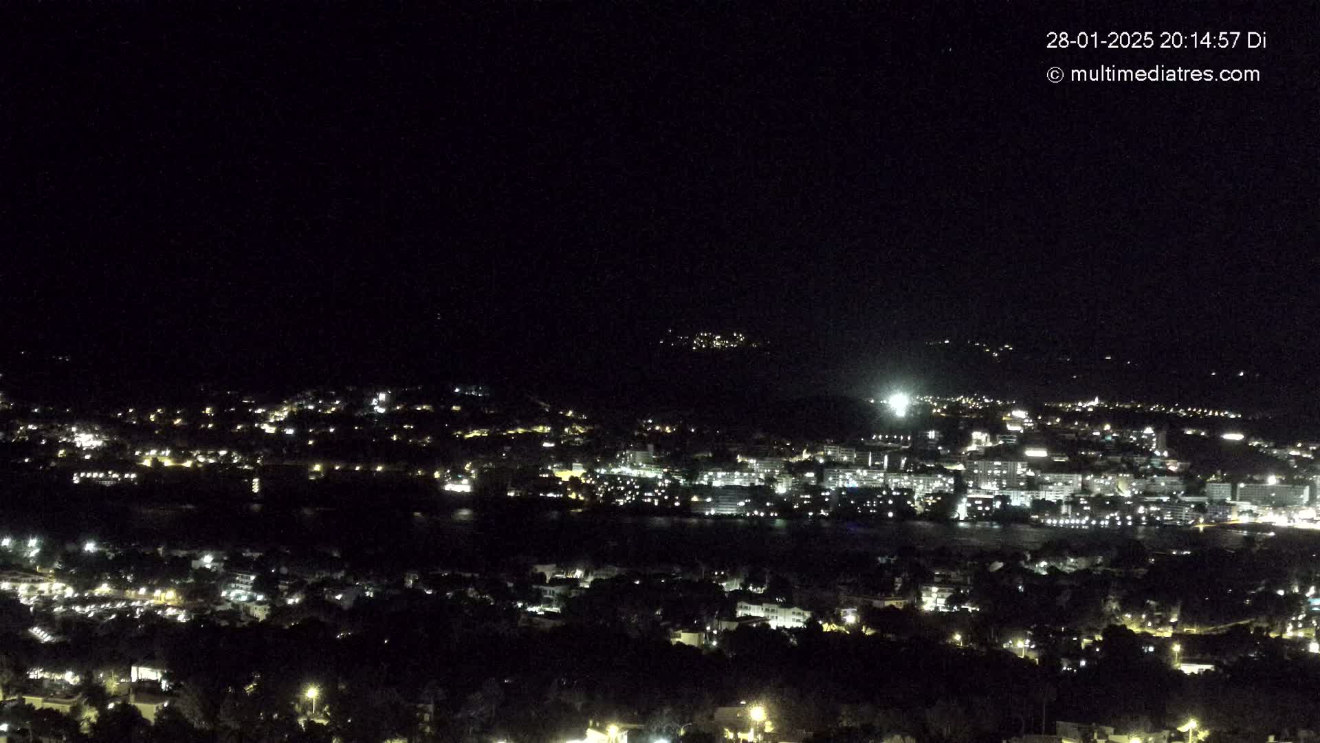 A nighttime, aerial view of a city illuminated by many lights, situated near a body of water under a clear, dark sky.
