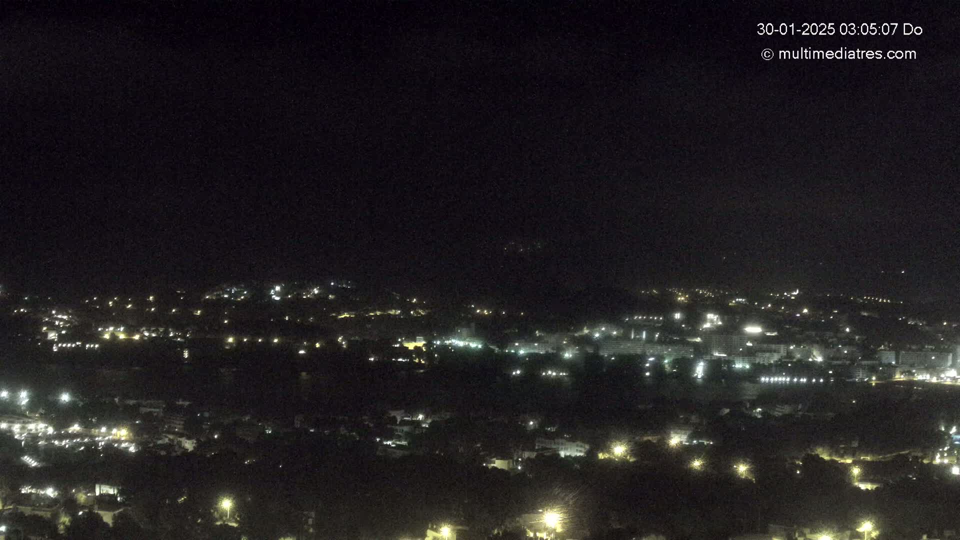 A nighttime, high-angle view shows a sprawling town illuminated by scattered lights under a clear, dark sky.