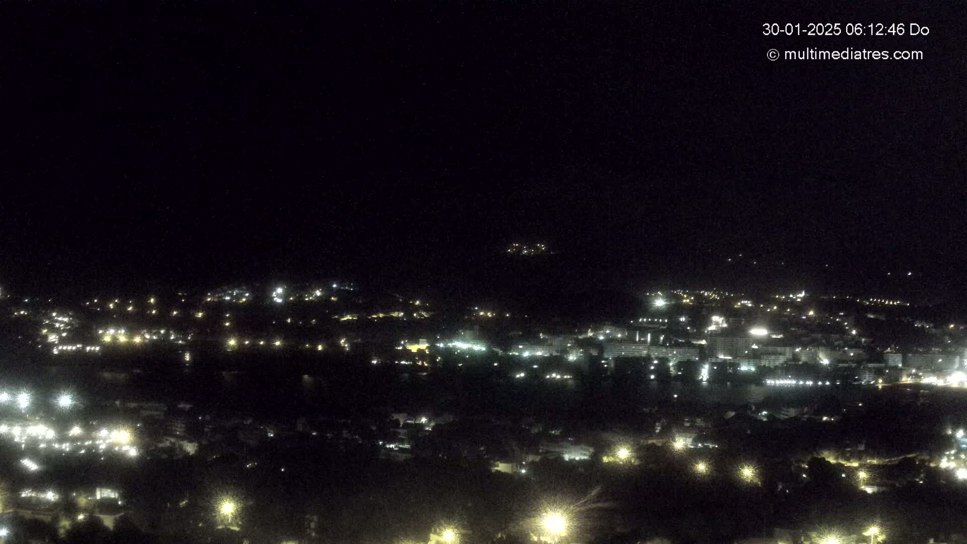 A nighttime, high-angle view of a town illuminated by many lights, spread across a hillside.