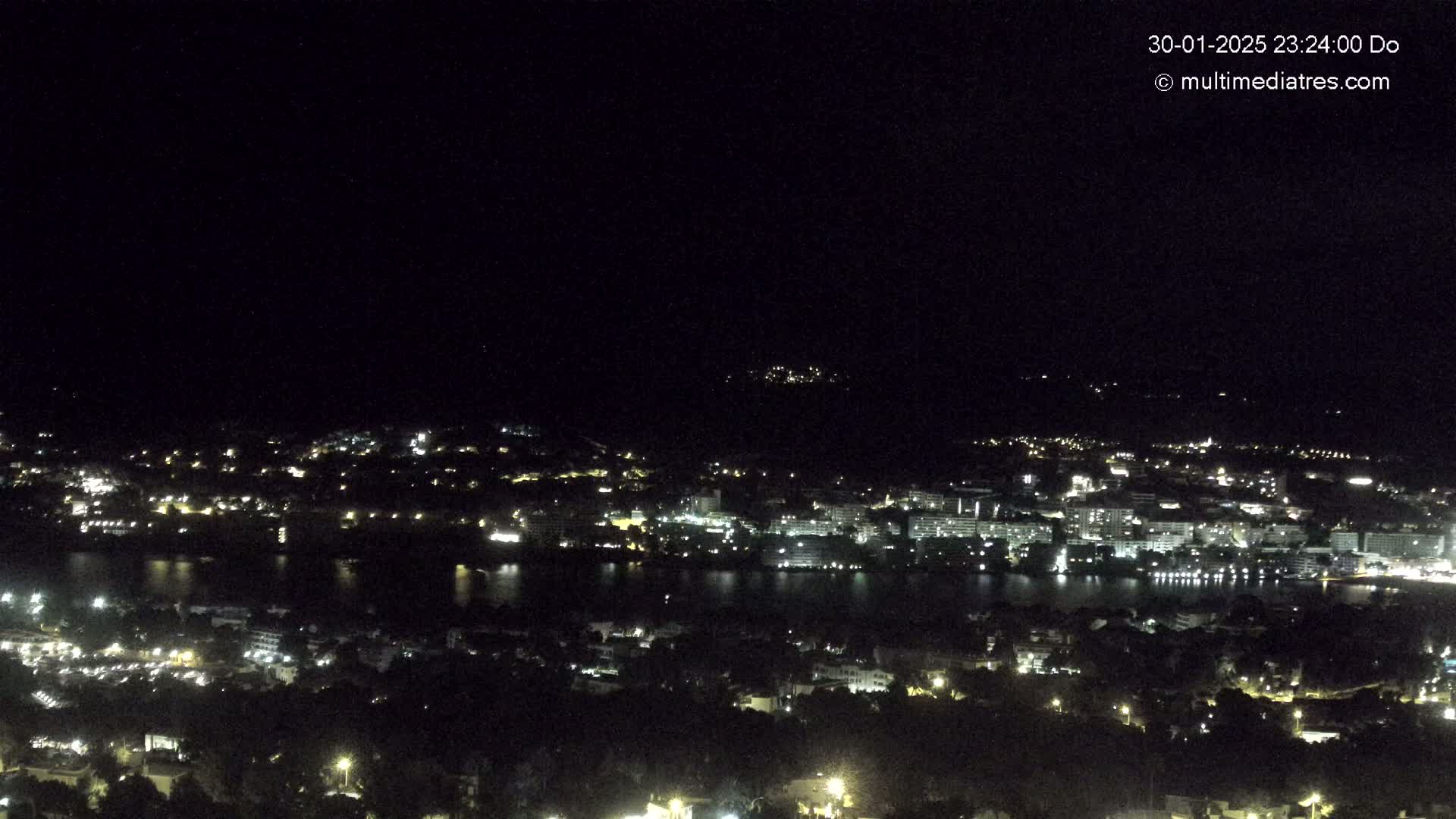 A nighttime, aerial view of a city sprawling along a body of water, illuminated by scattered lights.