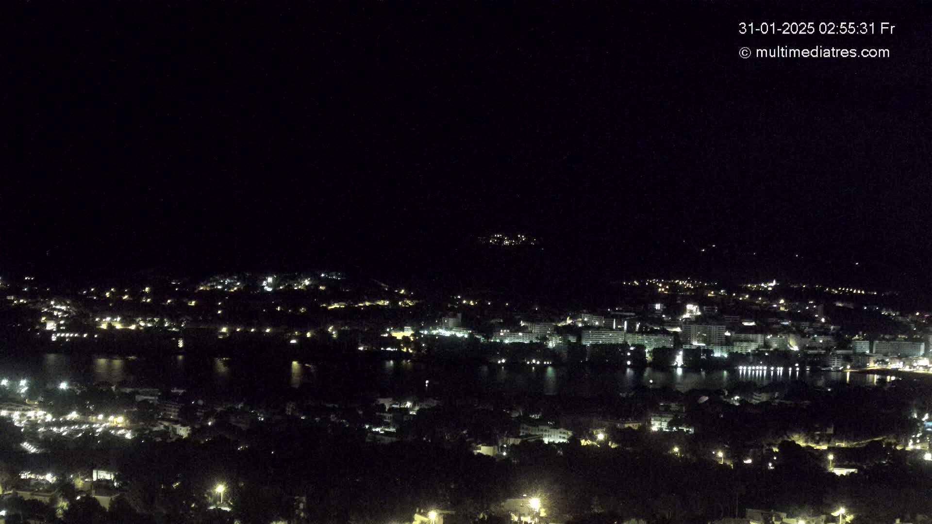 A nighttime, aerial view of a city illuminated by lights, situated beside a dark body of water.