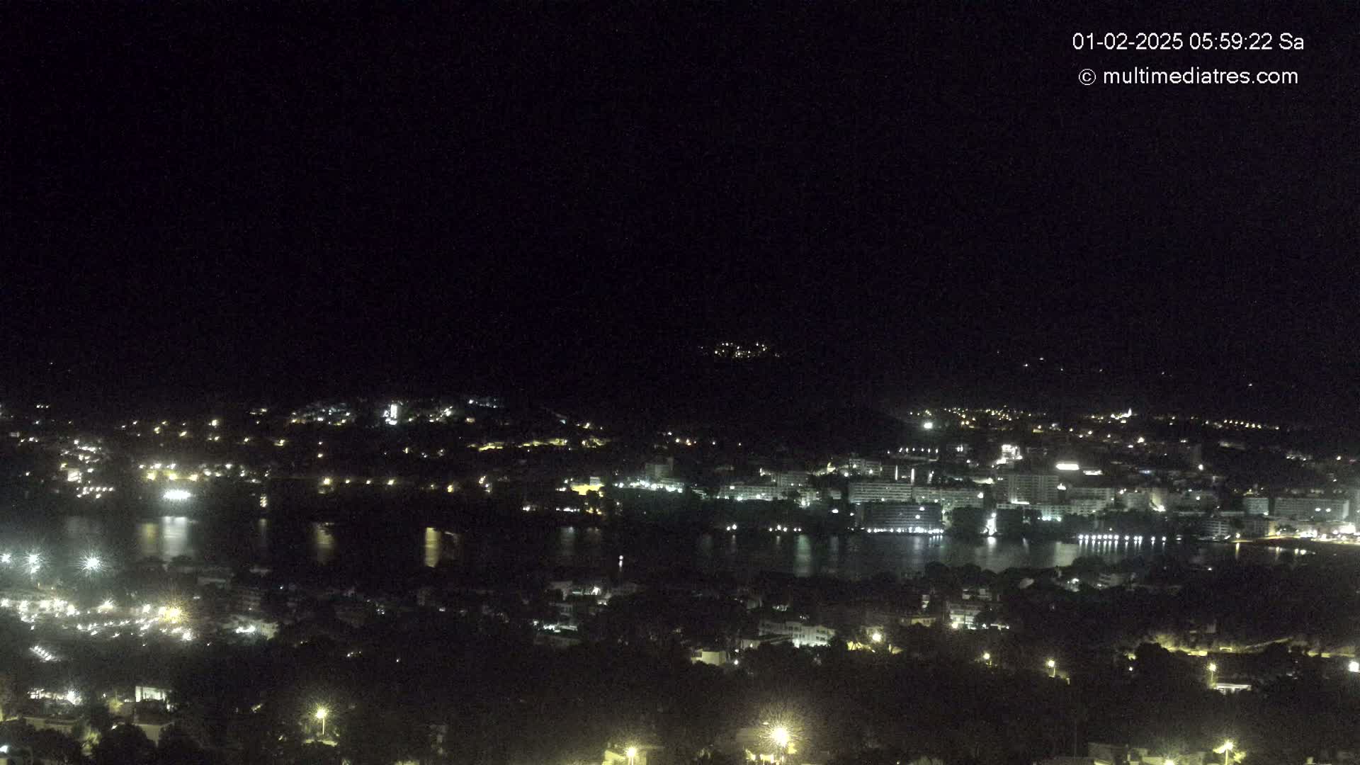 A nighttime, high-angle view shows a city illuminated by lights surrounding a dark body of water.