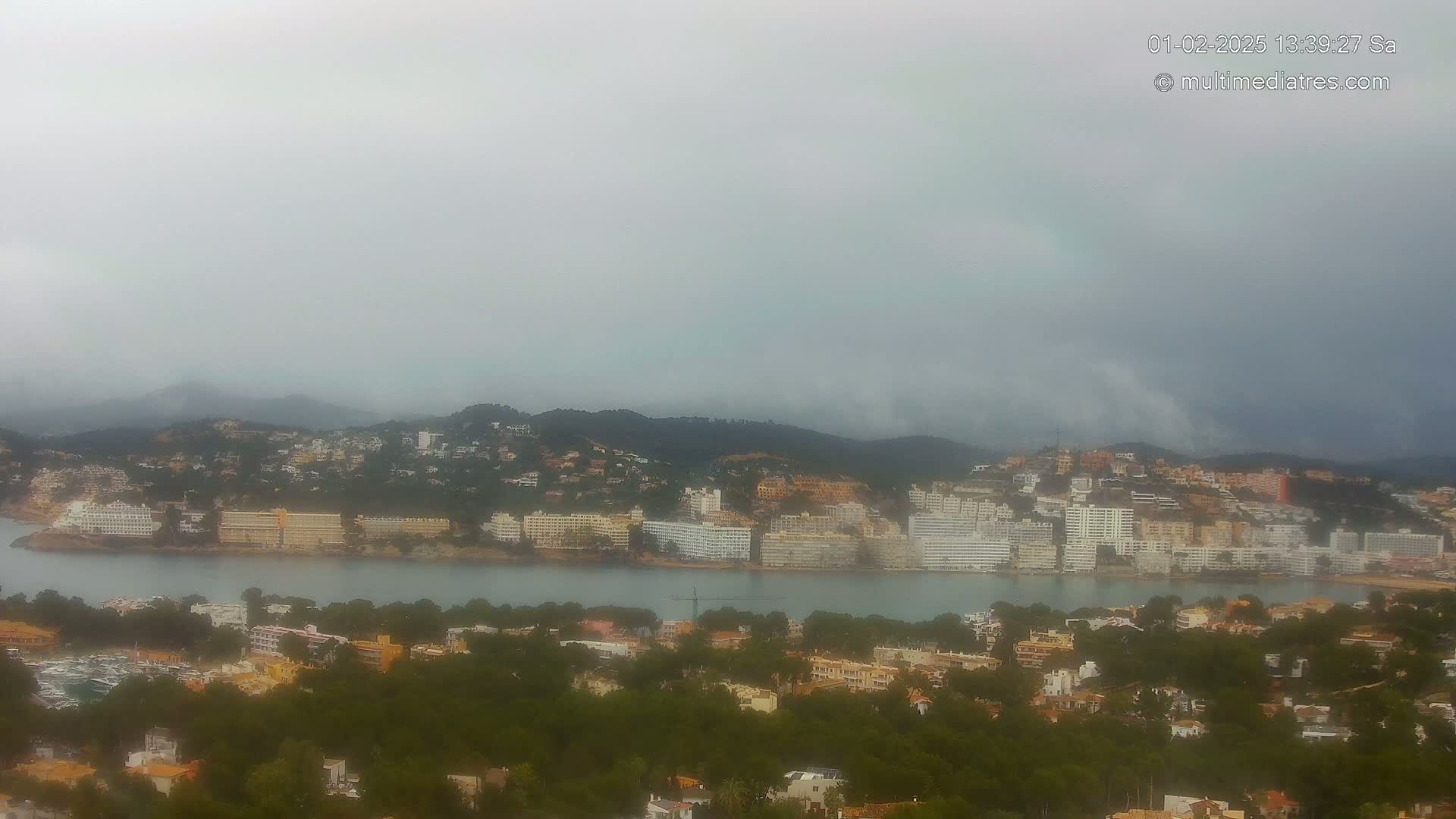 A coastal town nestled among hills is shrouded in a hazy, overcast sky.