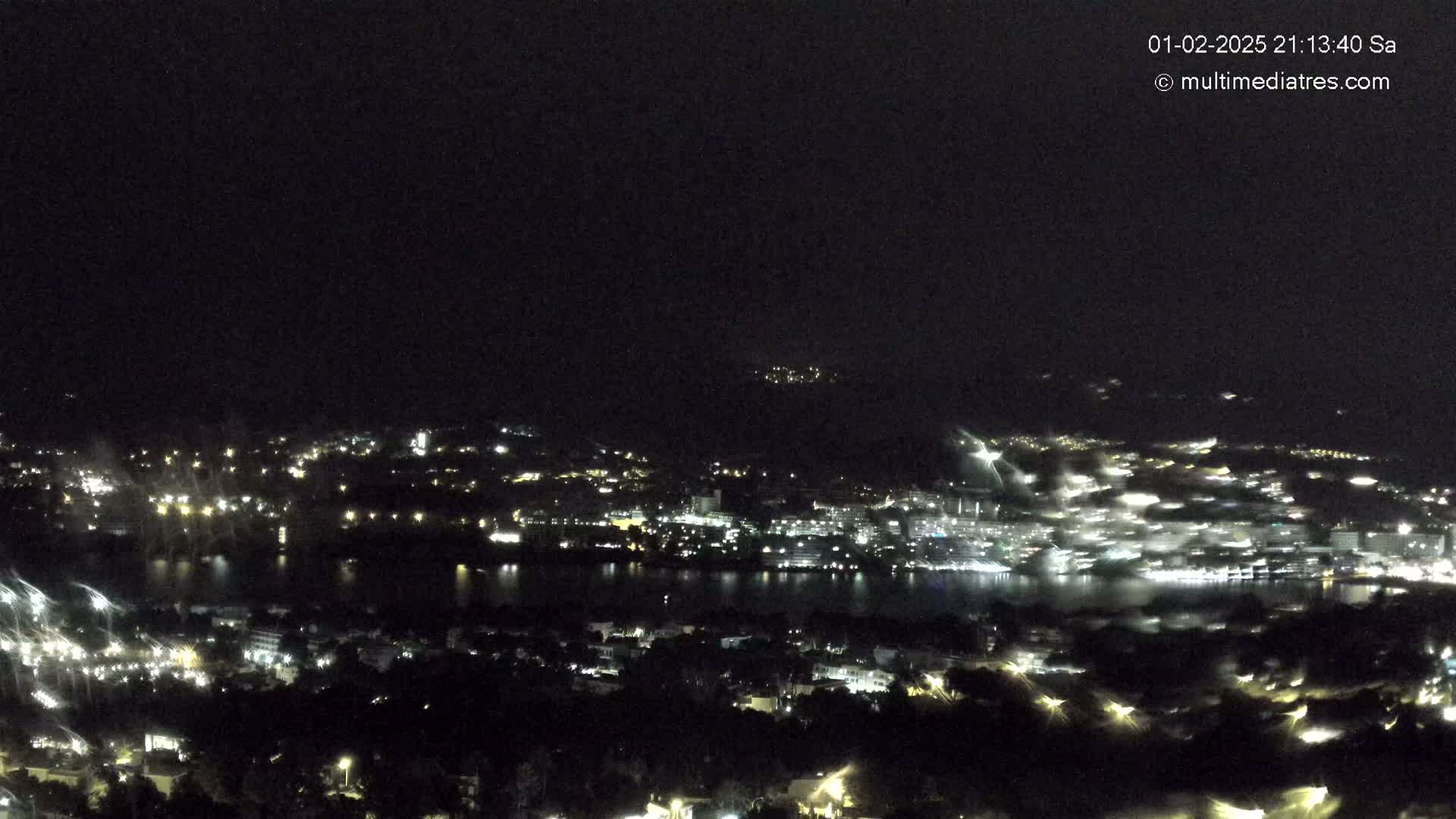 A nighttime view of a city and body of water with lightning striking in the distance.